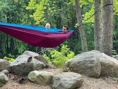 A man and a child are laying in a hammock in the woods.