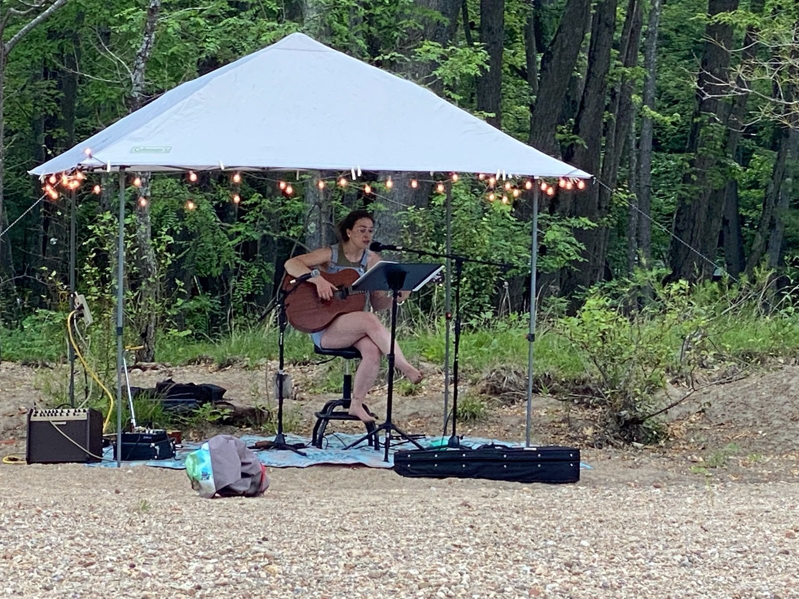 A woman is sitting under a tent playing a guitar and singing into a microphone.