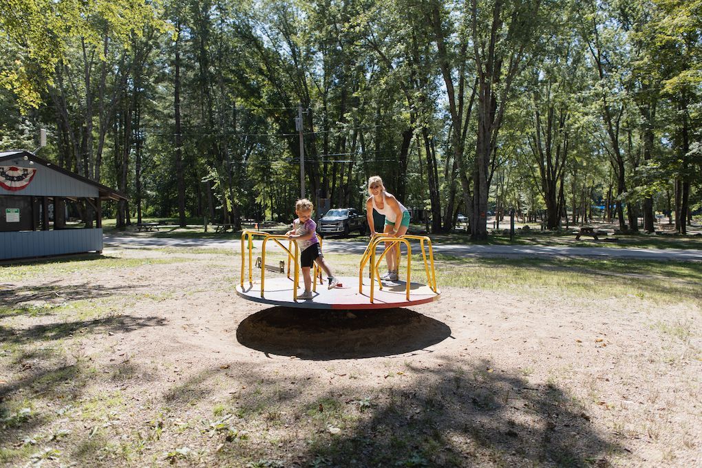 Two children are playing on a merry go round in a park.