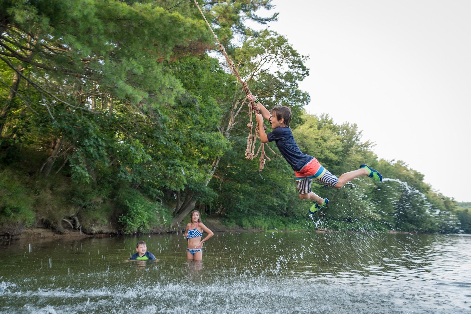 A boy is jumping off a rope swing into a river.