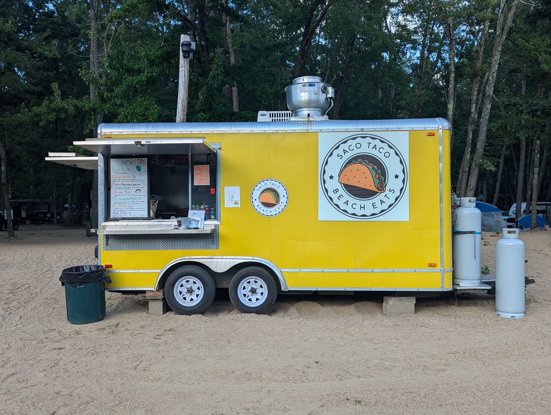 A yellow food truck with a taco on the side is parked in the dirt.