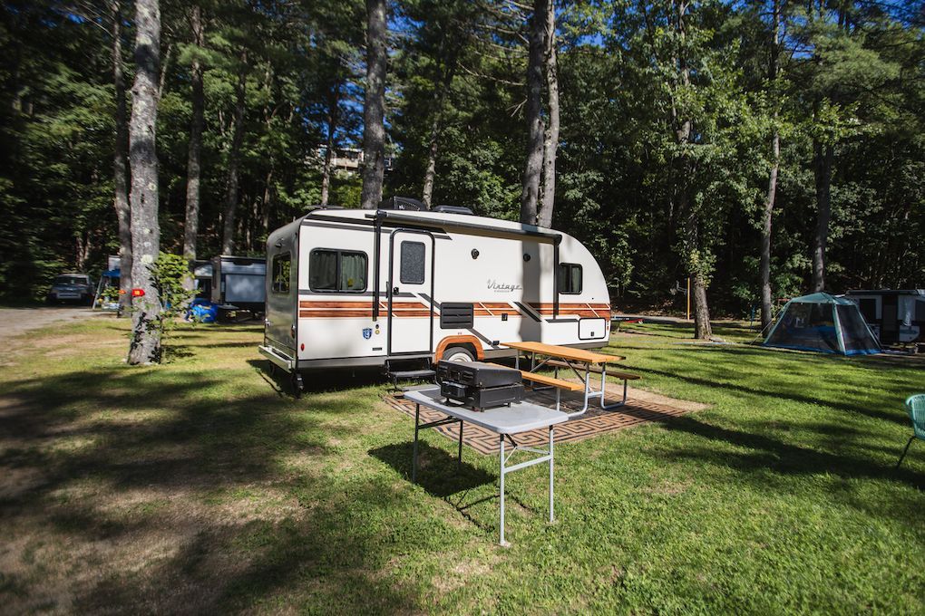 A rv is parked in a campground with a picnic table.