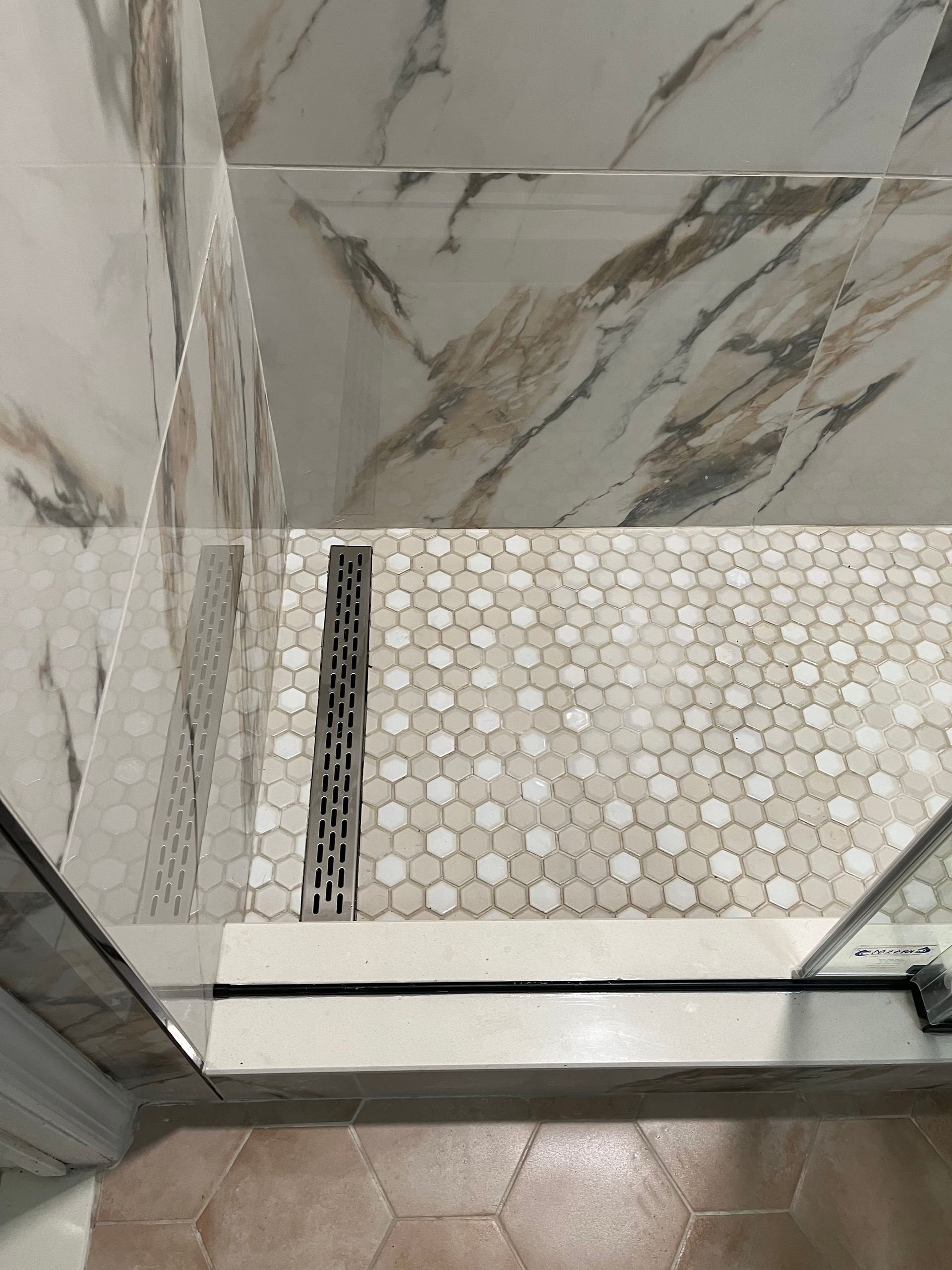 Shower with white and tan marble-look walls, mosaic tile floor, and a linear drain.