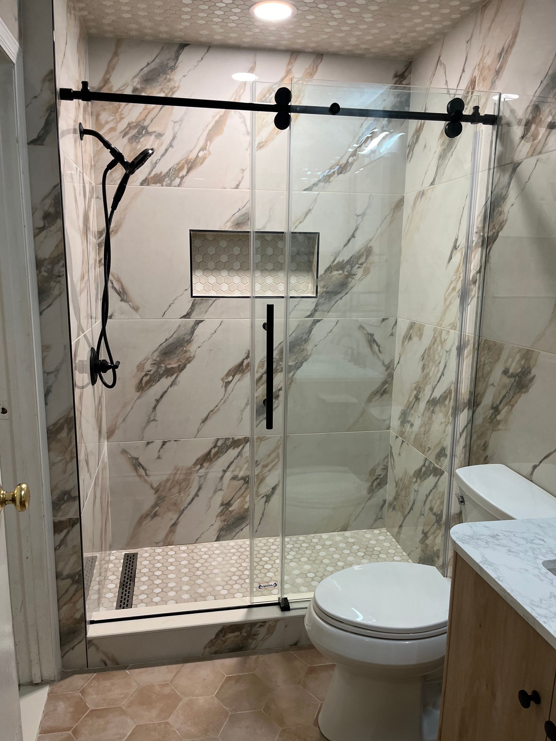 Bathroom with glass shower door, black hardware, marble-look tile, and a toilet.