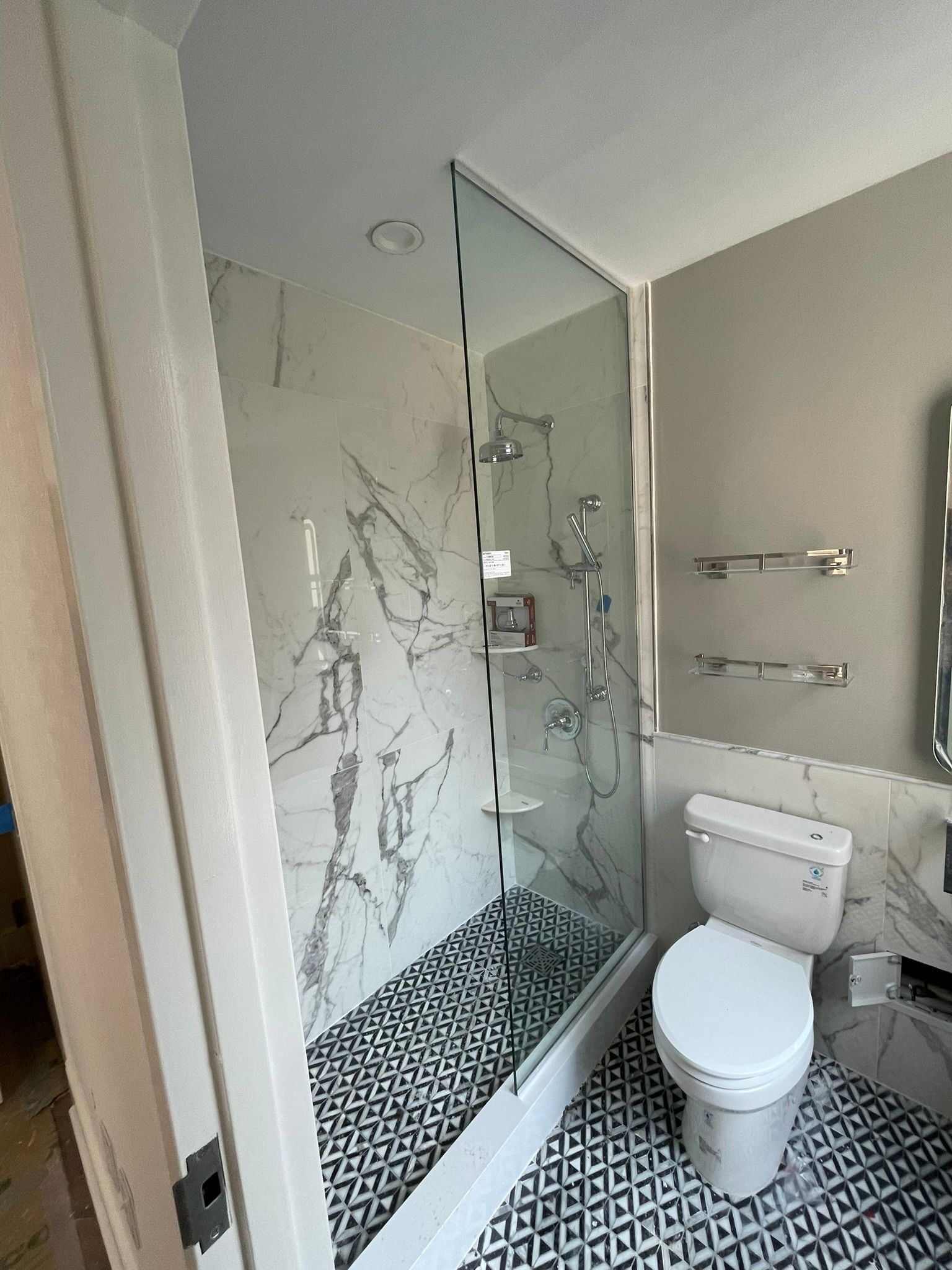 Bathroom with marble shower and black patterned floor. Toilet and towel racks are visible.