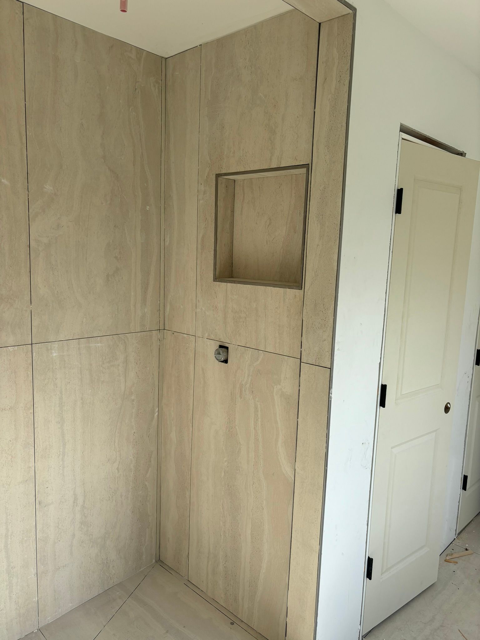 Bathroom wall with niche and partially installed tile, next to a white door.