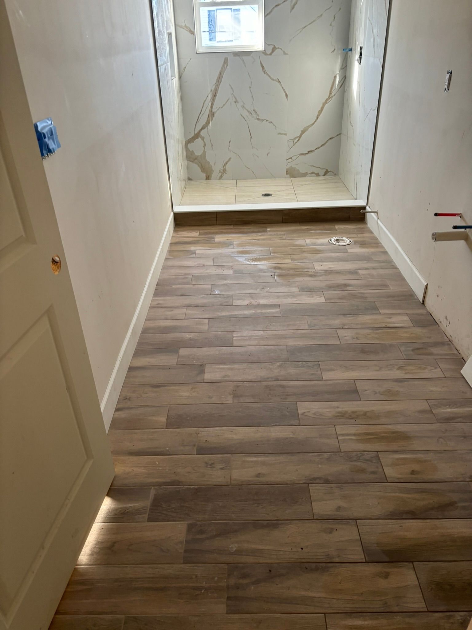 Bathroom with wood-look tile flooring leading to a marble-look tiled shower.