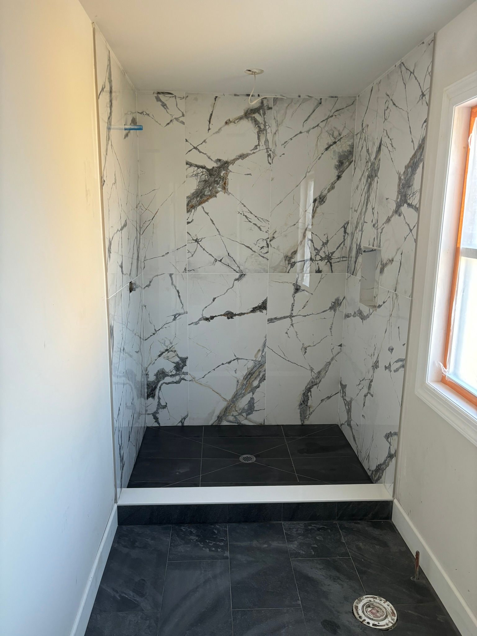 Bathroom shower stall with marble-patterned walls, black tile floor, and a raised step.
