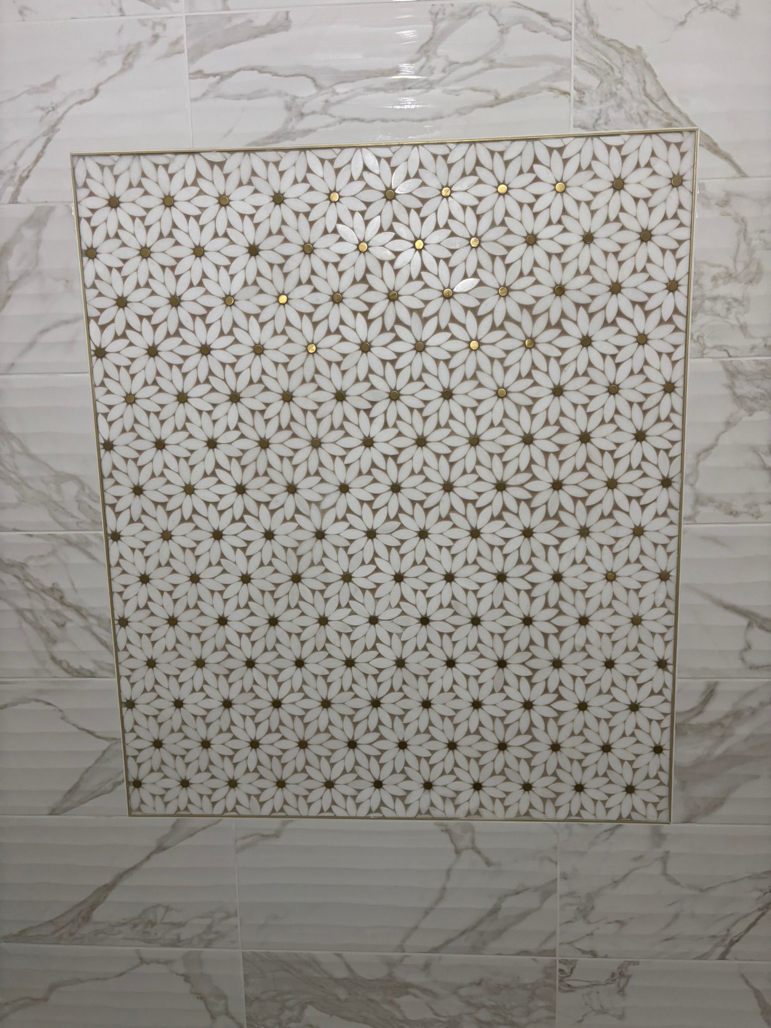 Decorative tile inset featuring a white and gold floral pattern, surrounded by marble-look tiles.