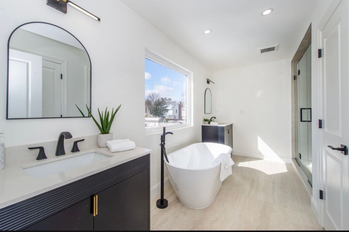 Modern white bathroom with black accents, freestanding tub, vanity, and shower.