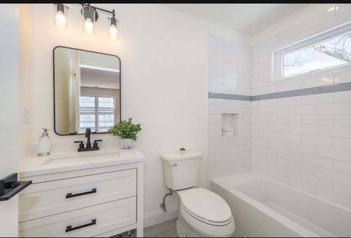White bathroom with vanity, toilet, and bathtub. Black mirror and fixtures. White subway tile.