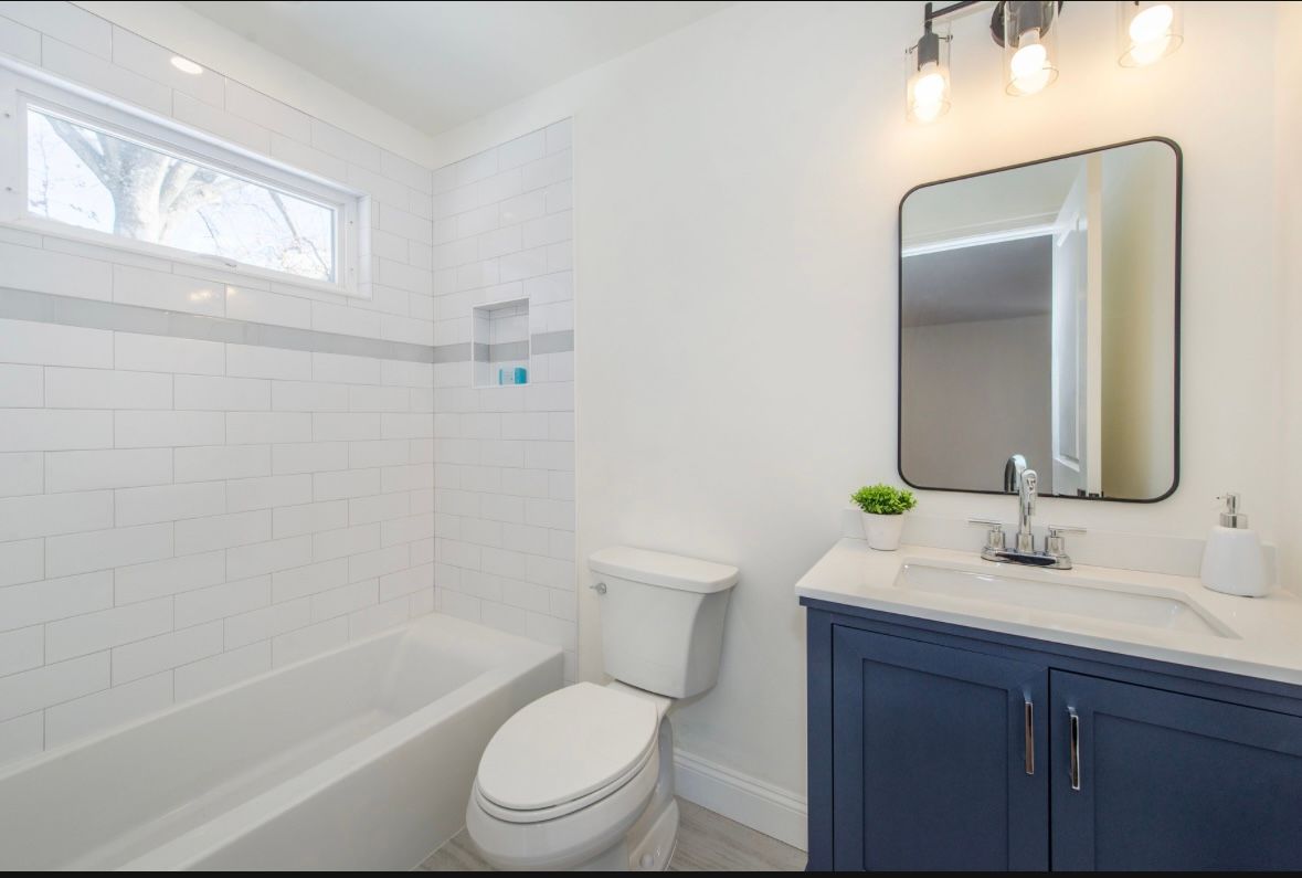 White bathroom with blue vanity and black framed mirror over sink.