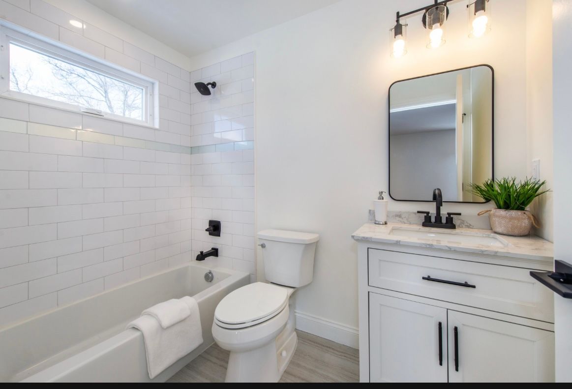 White bathroom with a tub, toilet, vanity, and black fixtures.