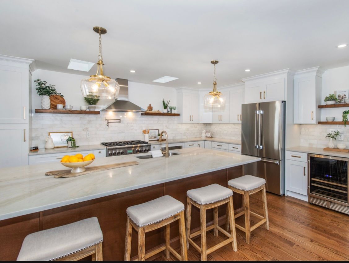 Modern kitchen with white cabinets, marble counters, a large island, and gold pendant lights.