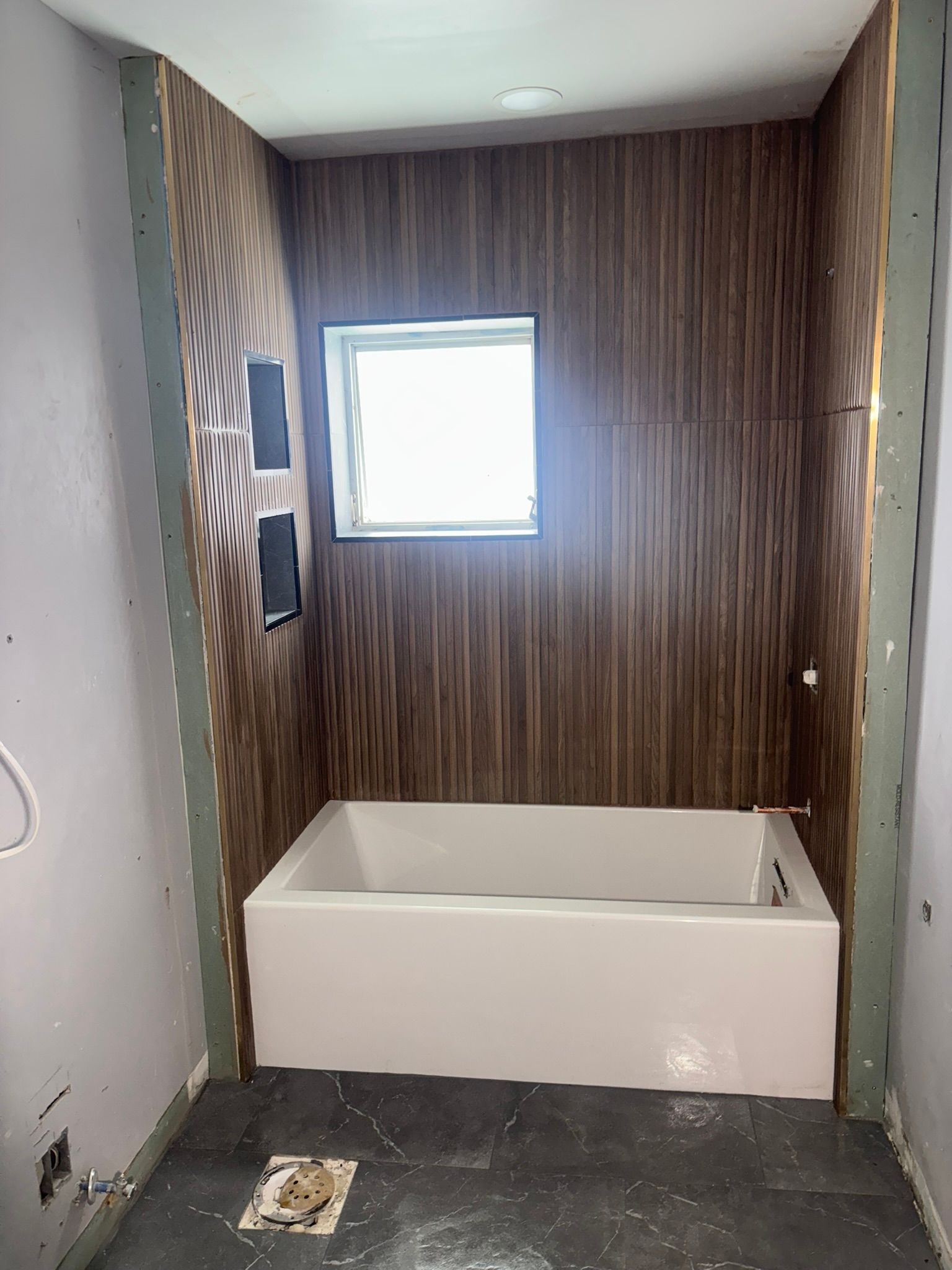 Bathroom with a white bathtub and wood-look paneling on the walls. A small window is centered above the tub.