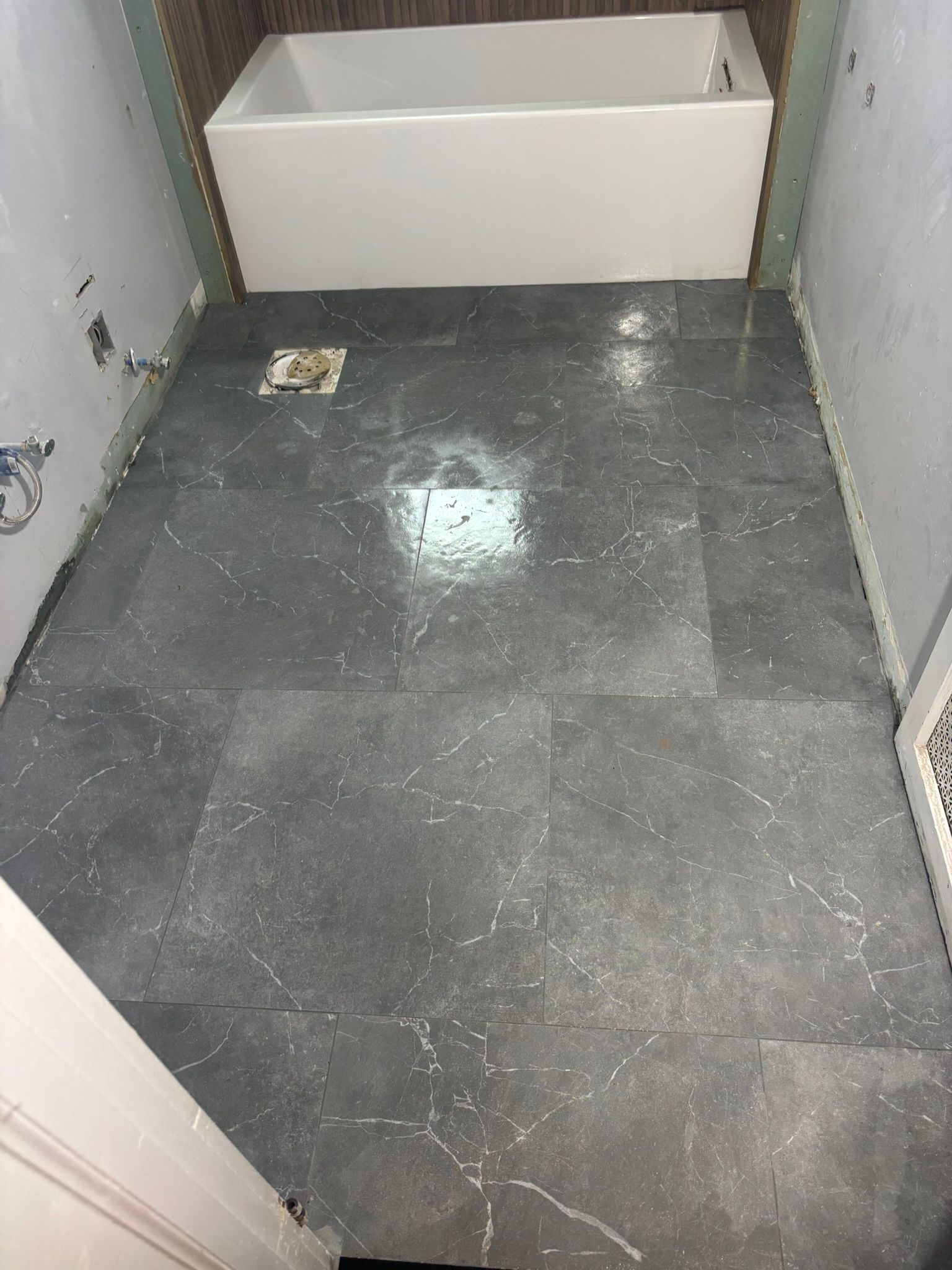 Bathroom floor tiled with dark gray stone; white bathtub at the back.