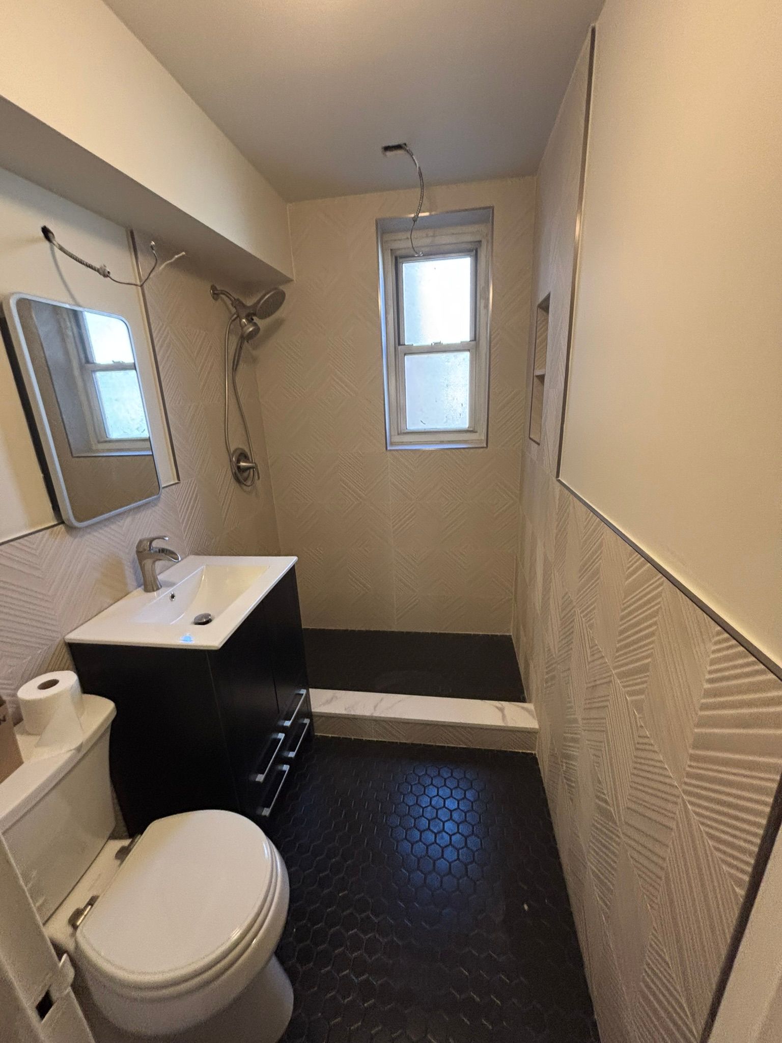 Small bathroom with black hexagon tile floor, white toilet, vanity, and shower.