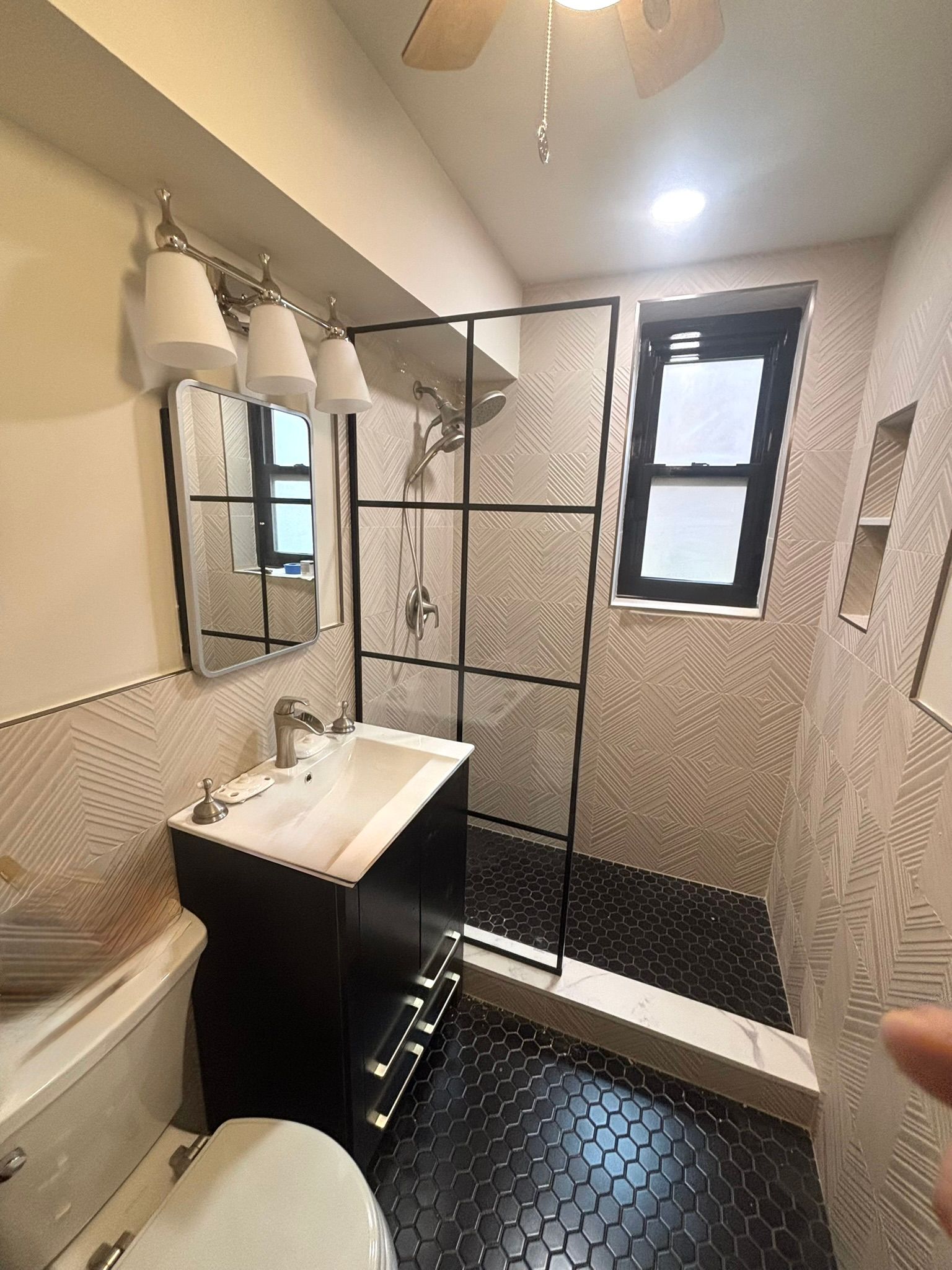 Small bathroom with black and white tile, shower with black frame, vanity, and toilet.