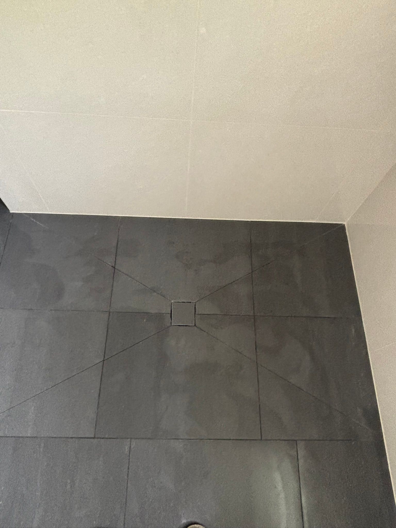 Black tiled shower floor with central drain, white ceiling, and gray walls.