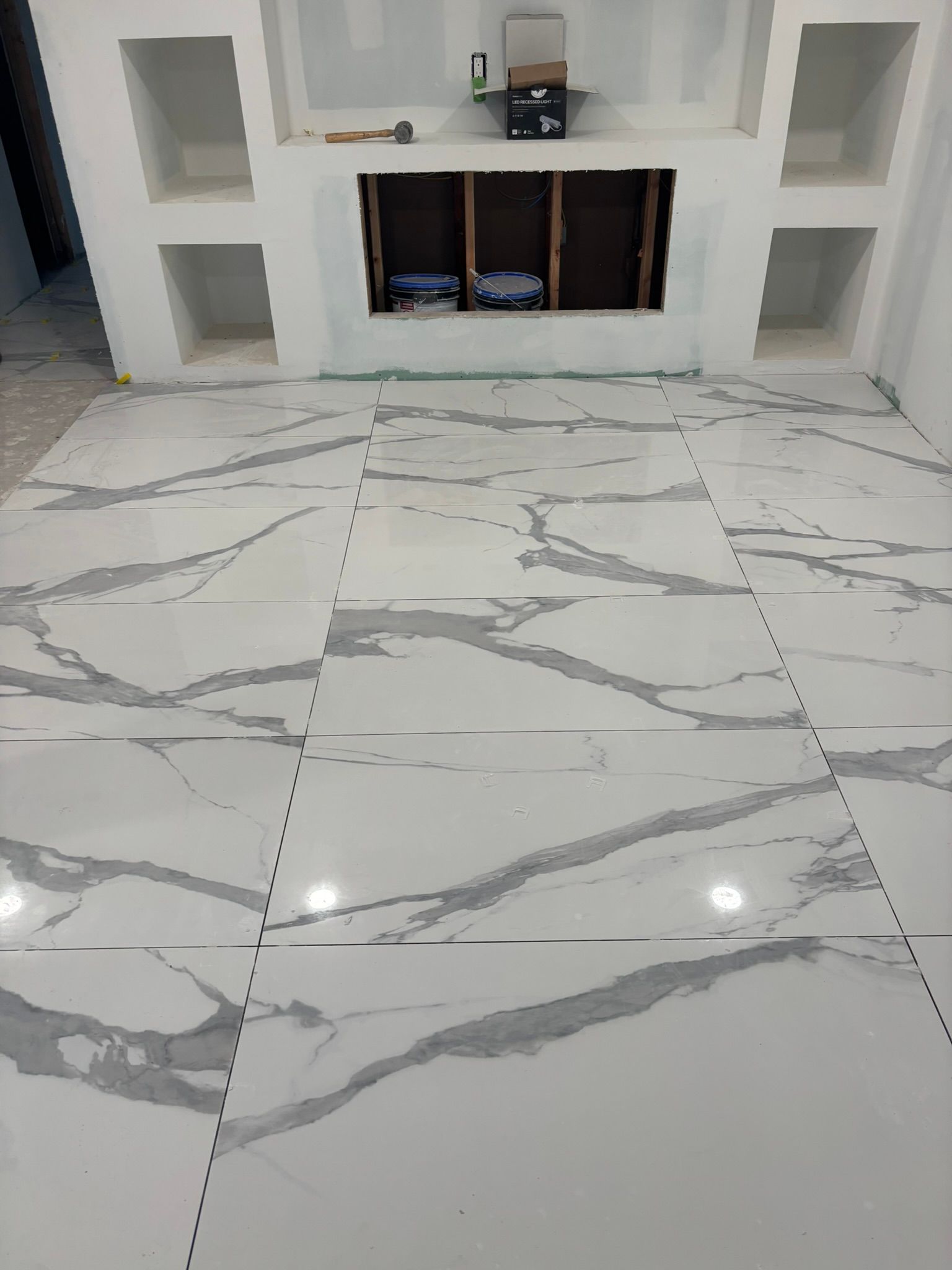 White marble-look tile flooring in a room under construction, with a partially built fireplace and shelves.