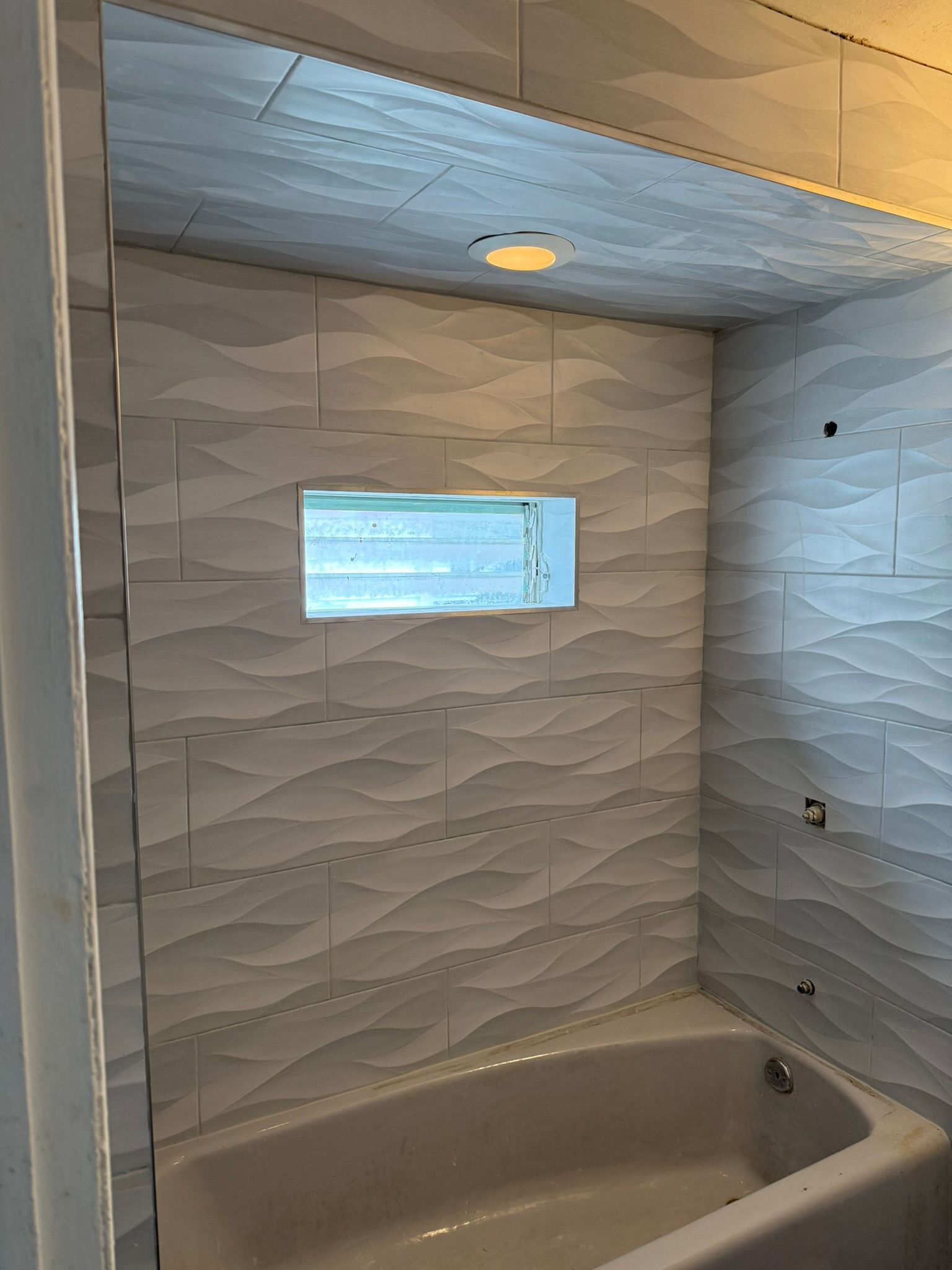 White tiled shower with a niche and built-in light above the bathtub.