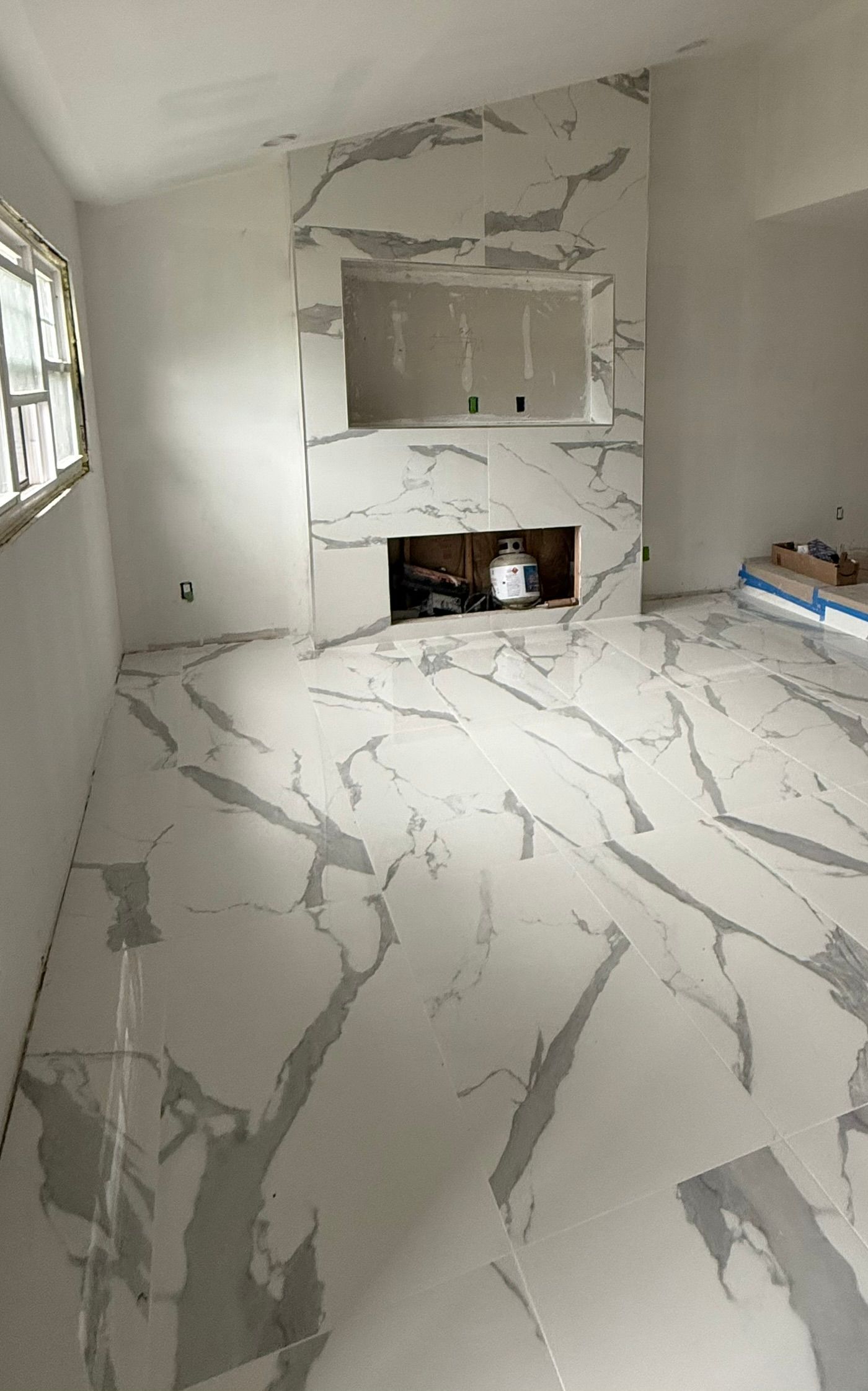 Room under construction with white marble tile floor and fireplace.