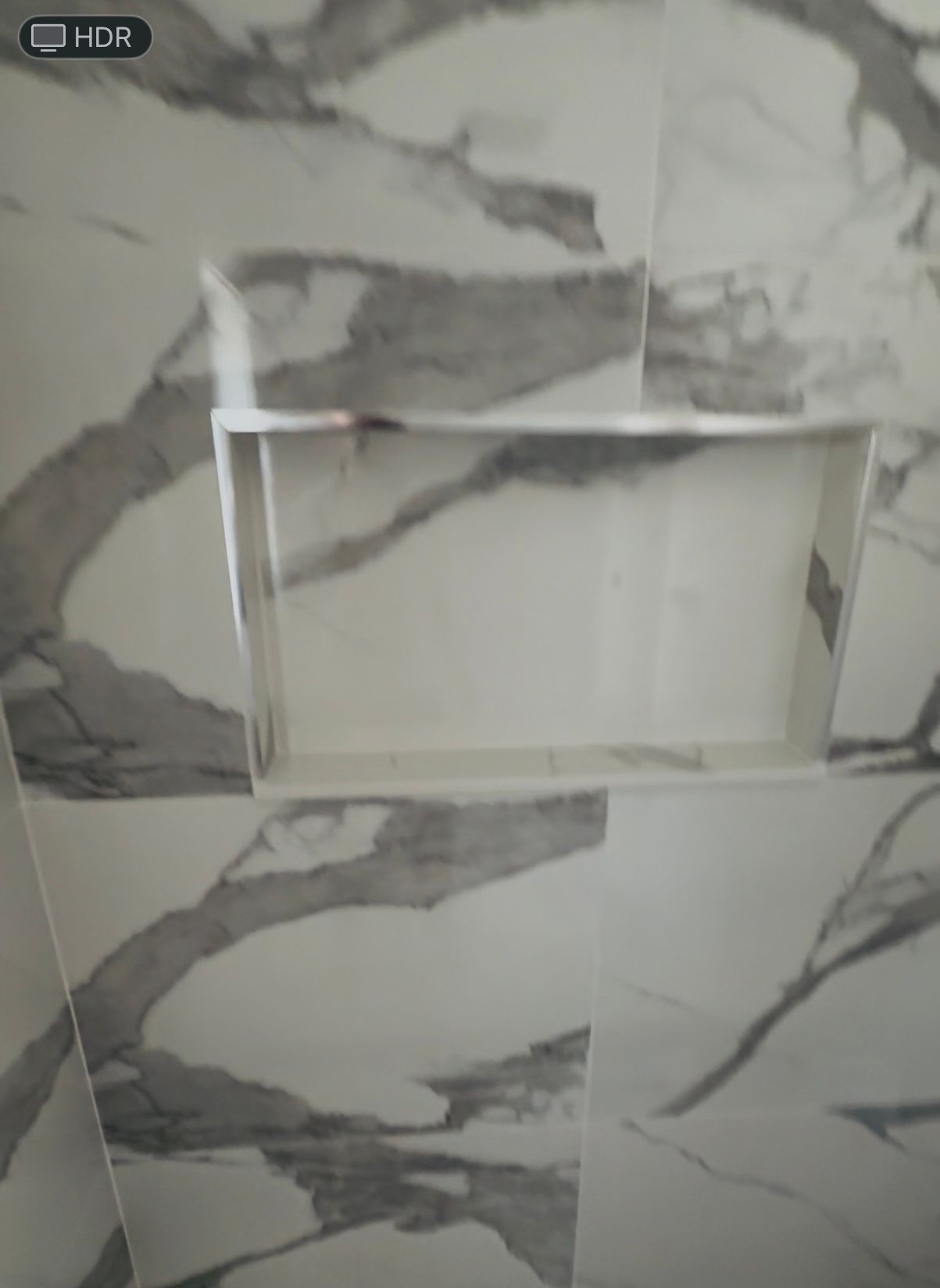 Shower wall with marble-patterned tile, featuring a built-in recessed shelf.