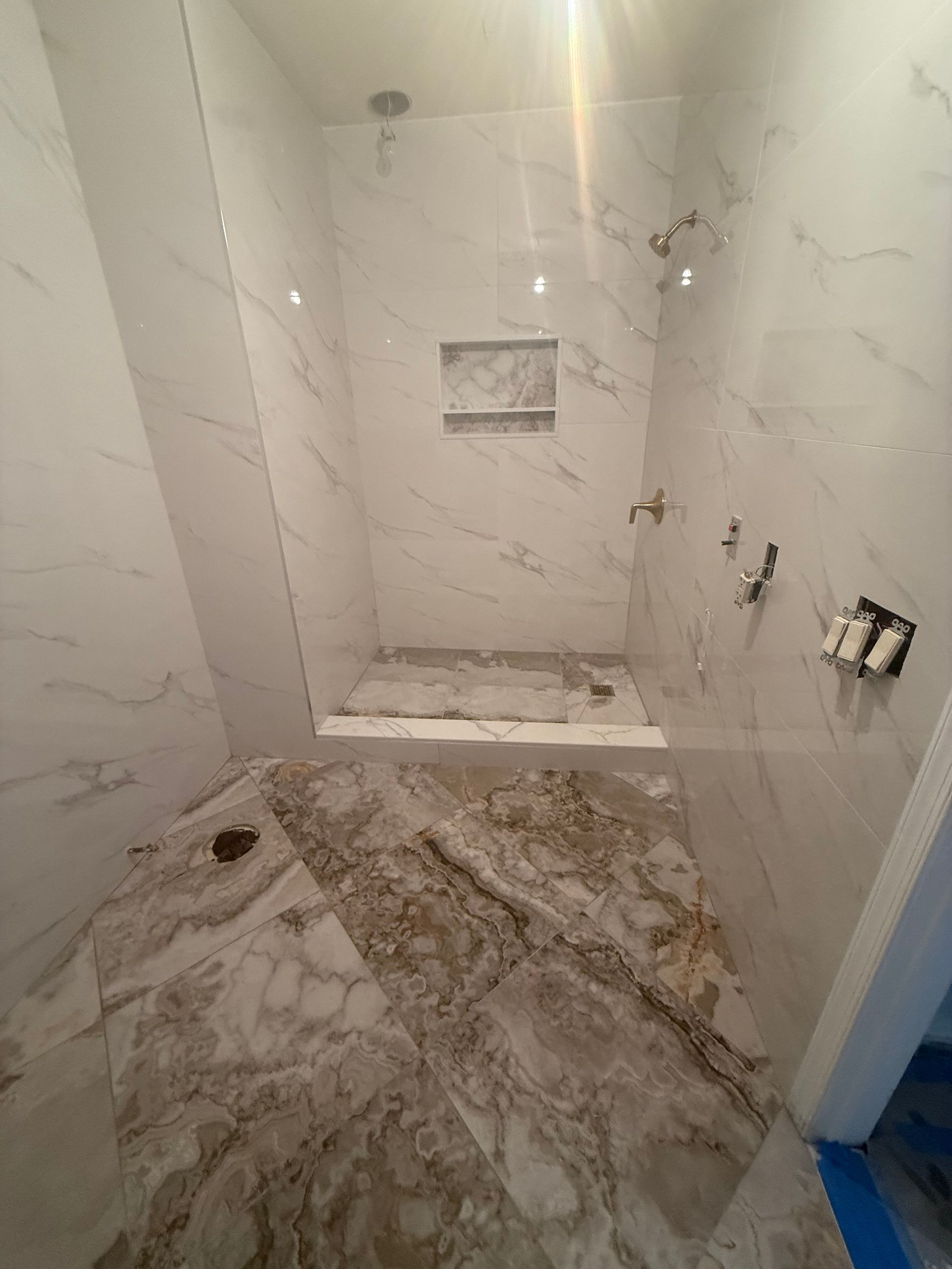 Bathroom under construction with white marble shower and floor tiles, unfinished.