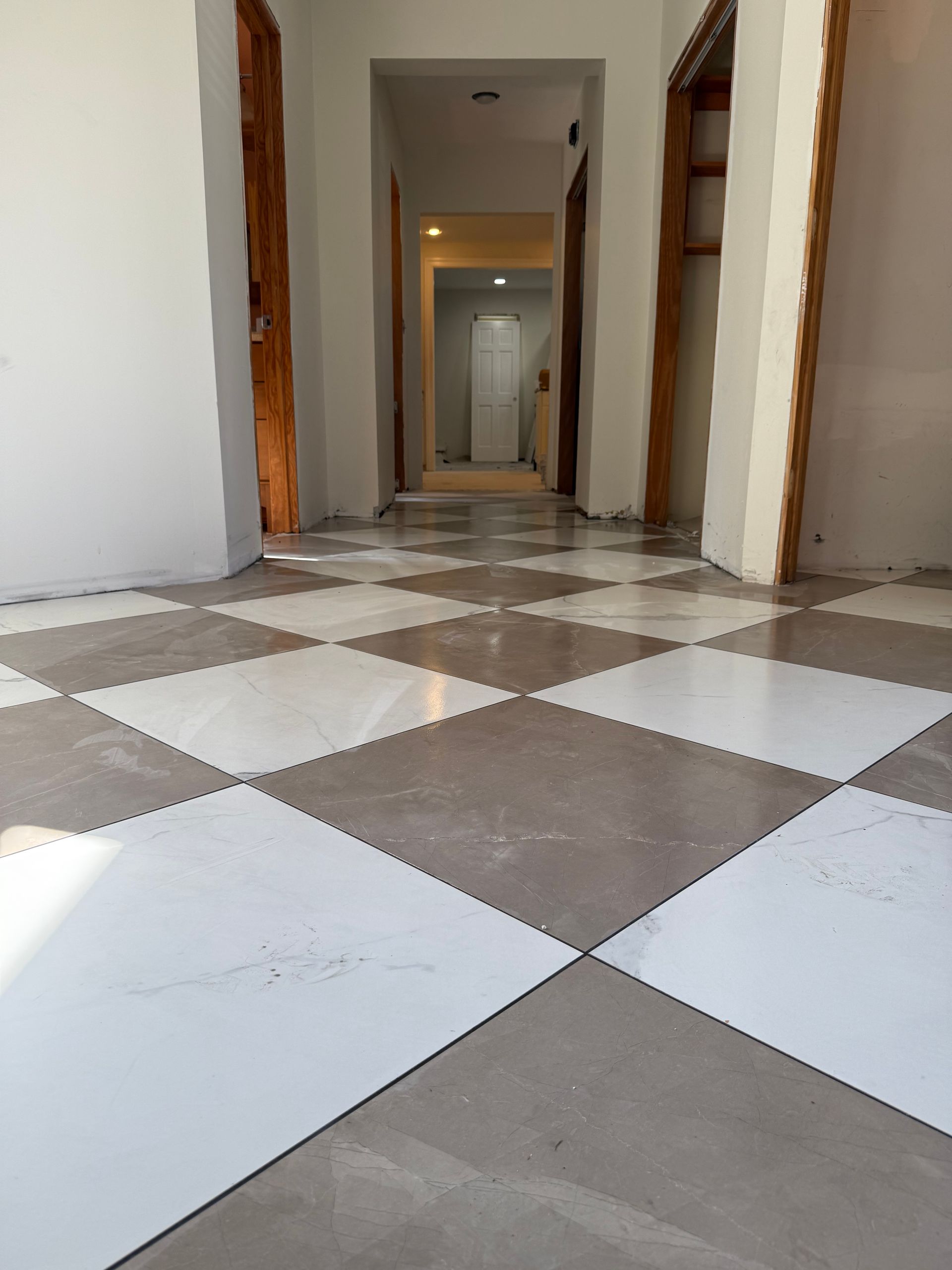 Diamond-patterned tile floor in a hallway with open doors and neutral-colored walls.