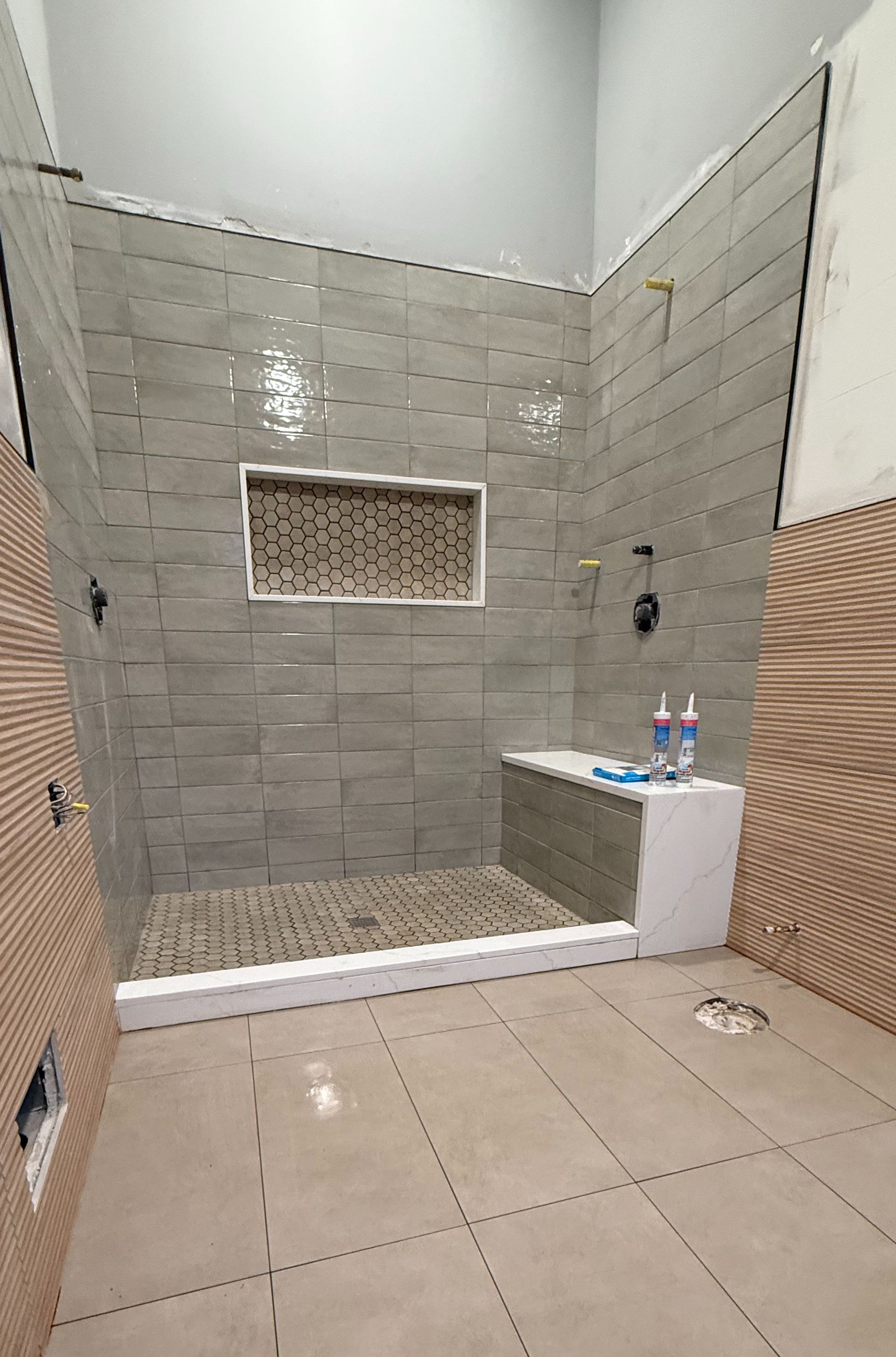 Newly tiled shower with built-in bench and recessed shelf. Grey and tan tones dominate.