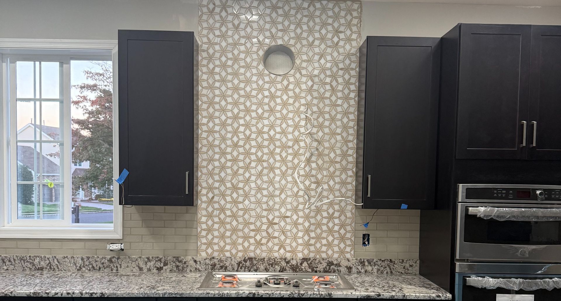 Kitchen with dark cabinets, patterned backsplash, granite countertop, and stainless steel oven.