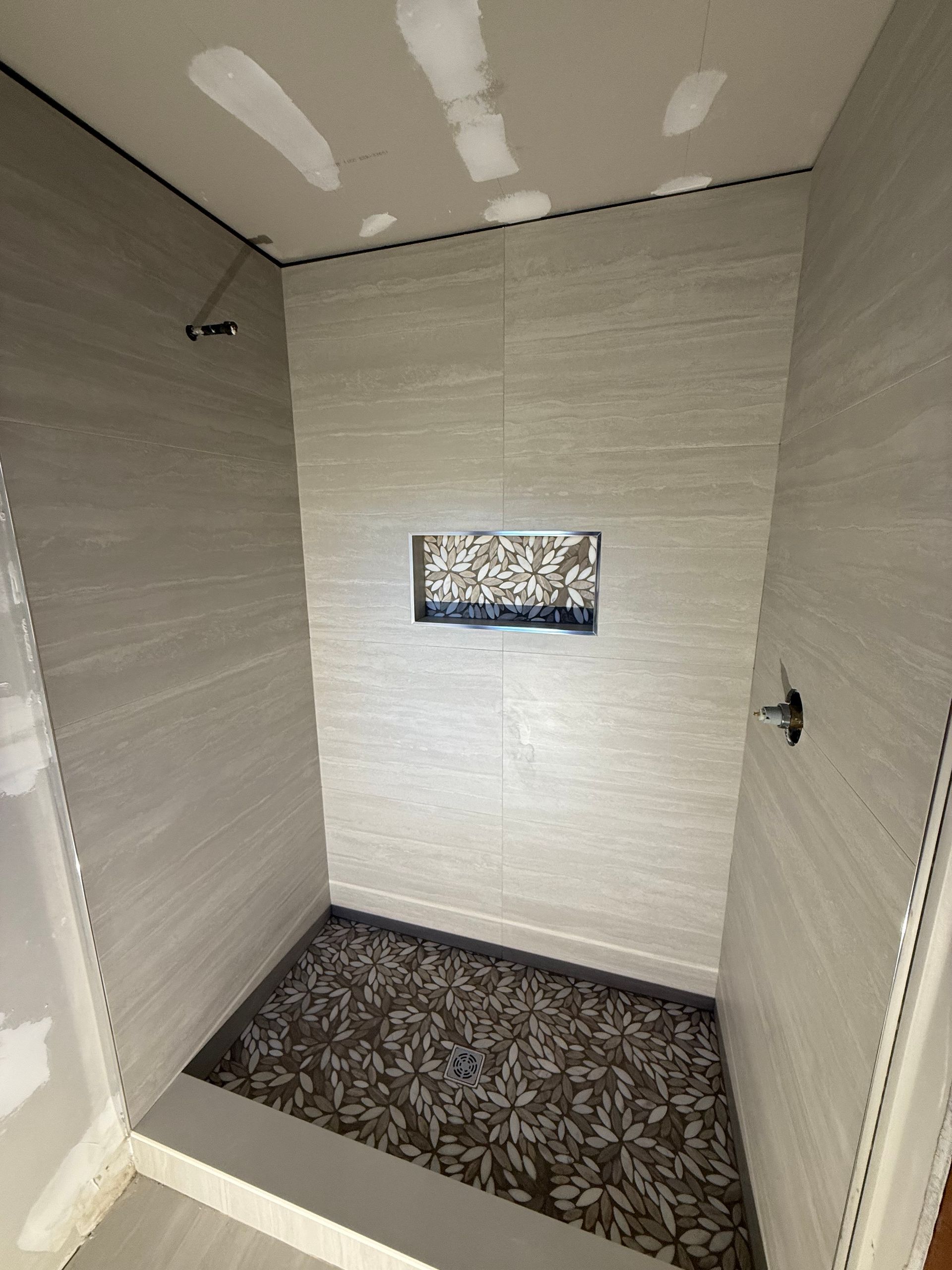 Shower stall with grey tiled walls, patterned floor, and built-in shelf.