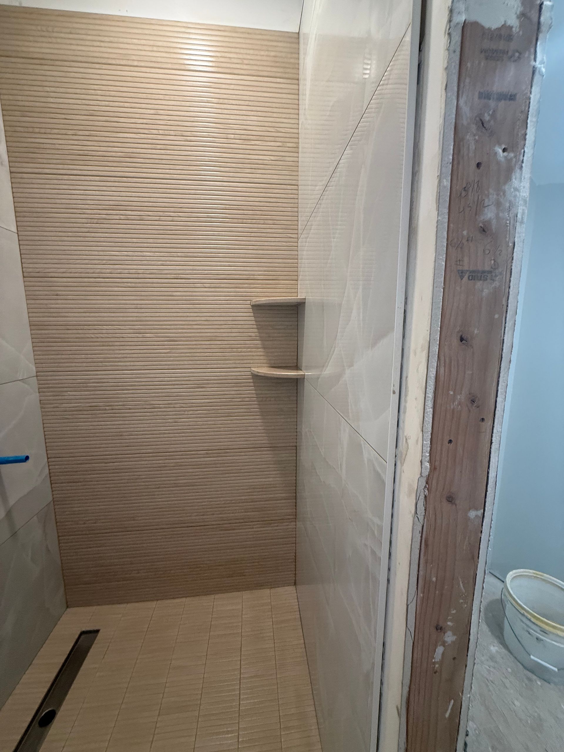 Shower stall with textured wall tiles and a built-in shelf, under construction.