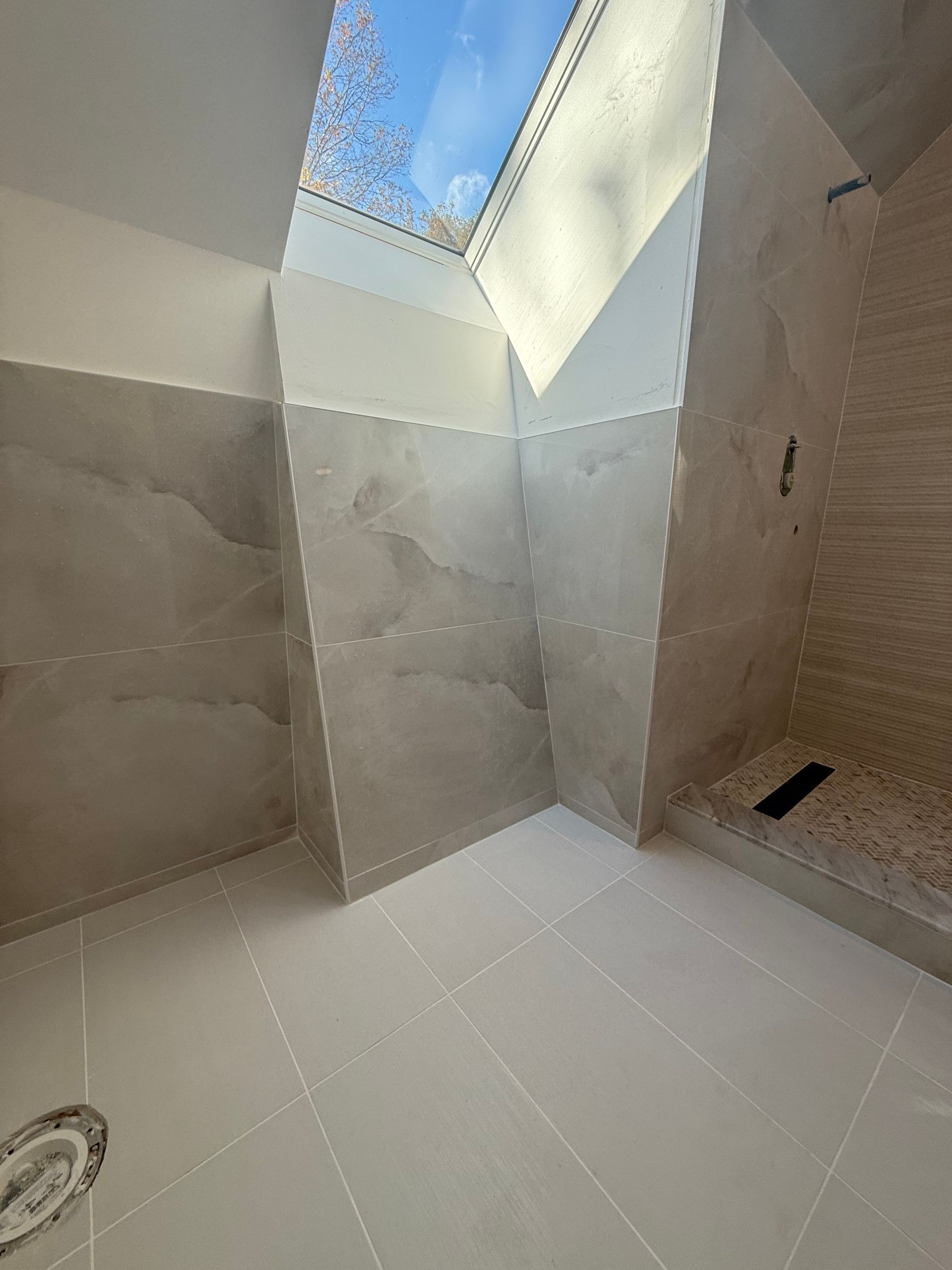 Modern shower with gray marble walls, white floor, and skylight.