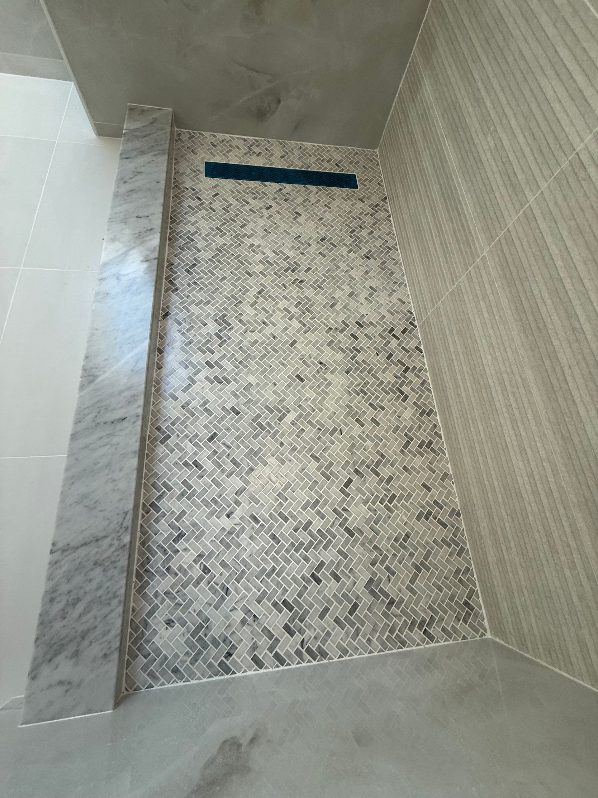 Shower stall with mosaic tile wall, marble trim, and linear drain.