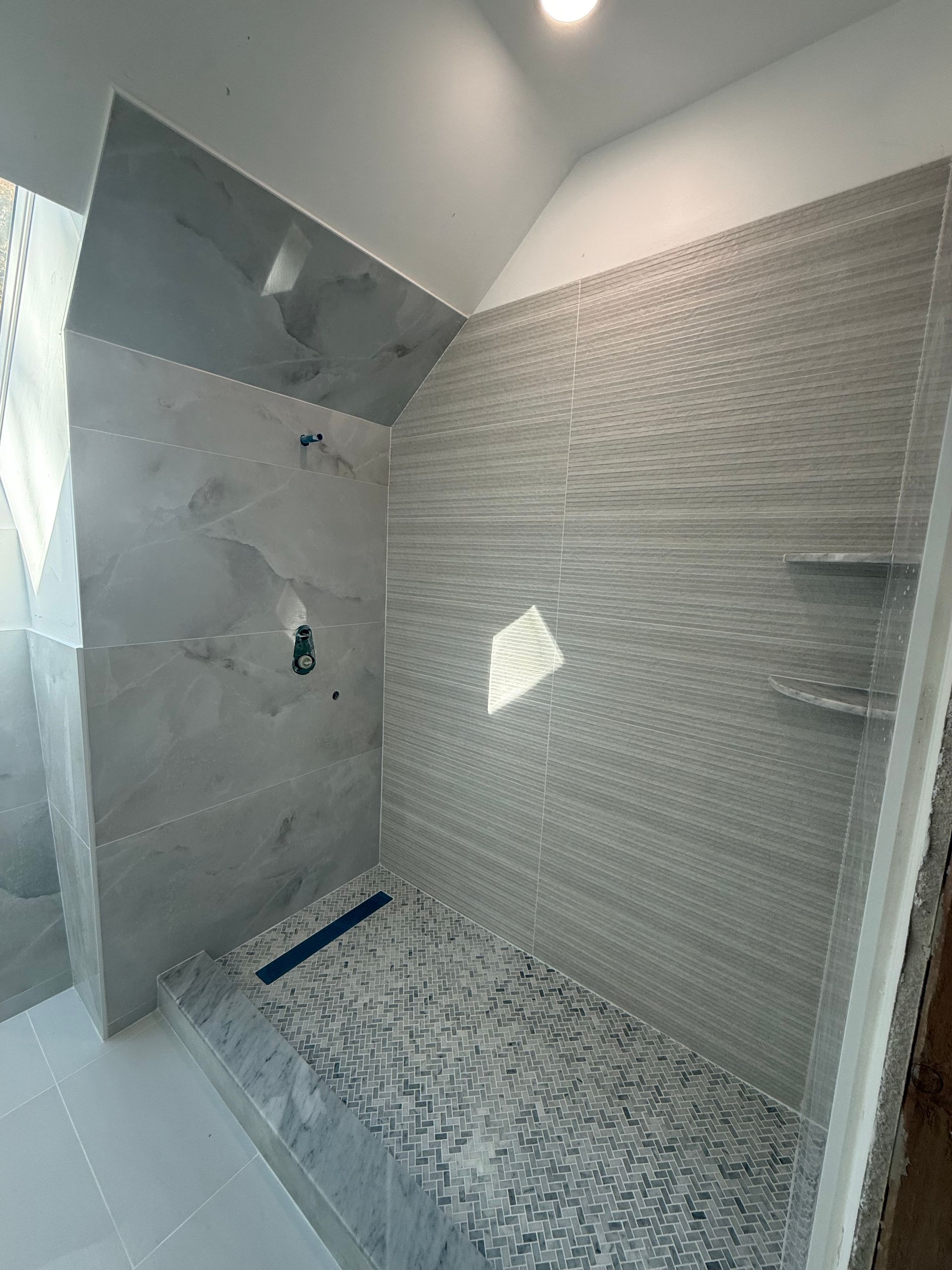 Tiled shower with gray and white marble, including built-in shelves.