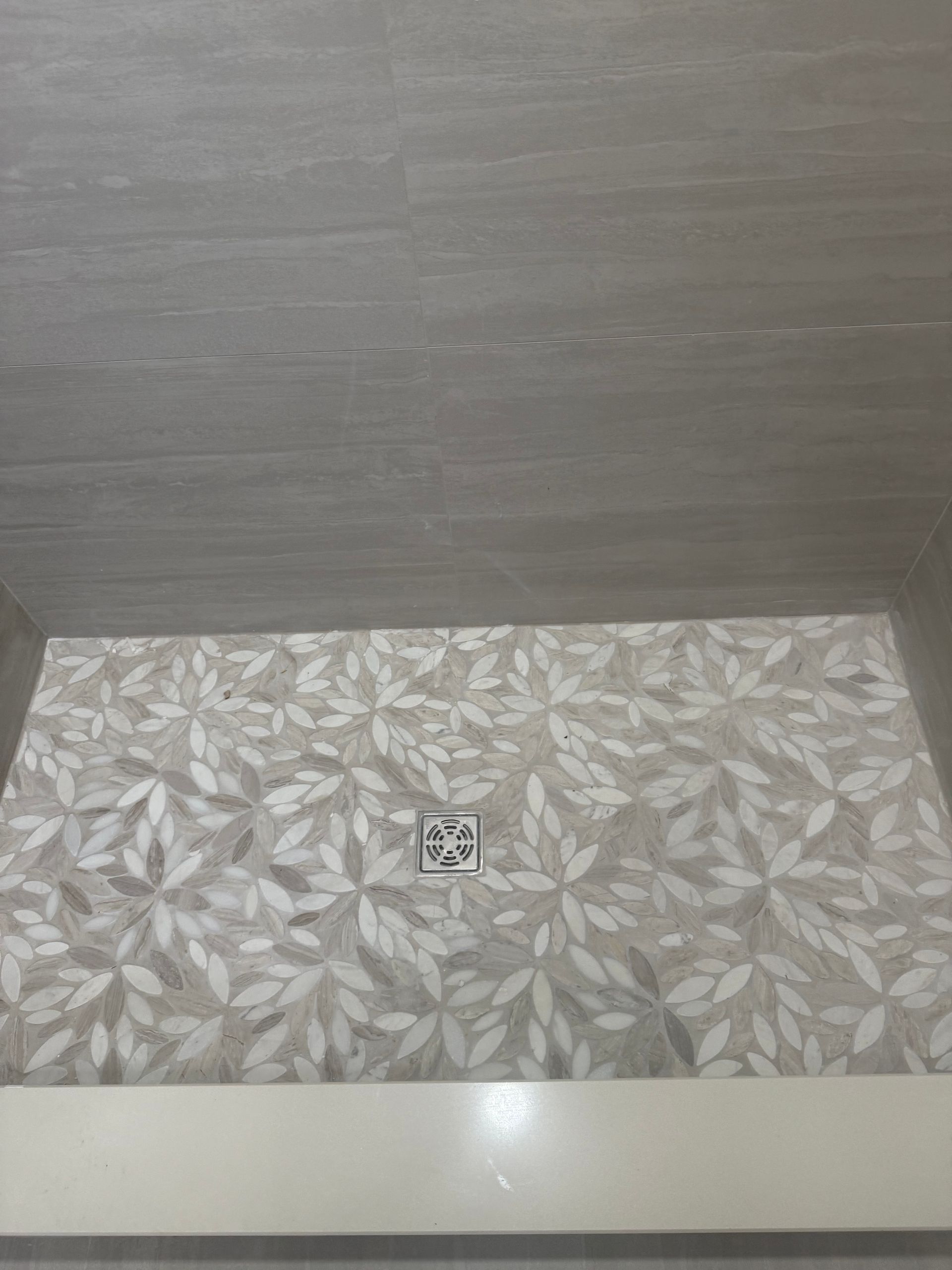 Shower with floral tile floor and gray walls, drain in the center, and a white curb.