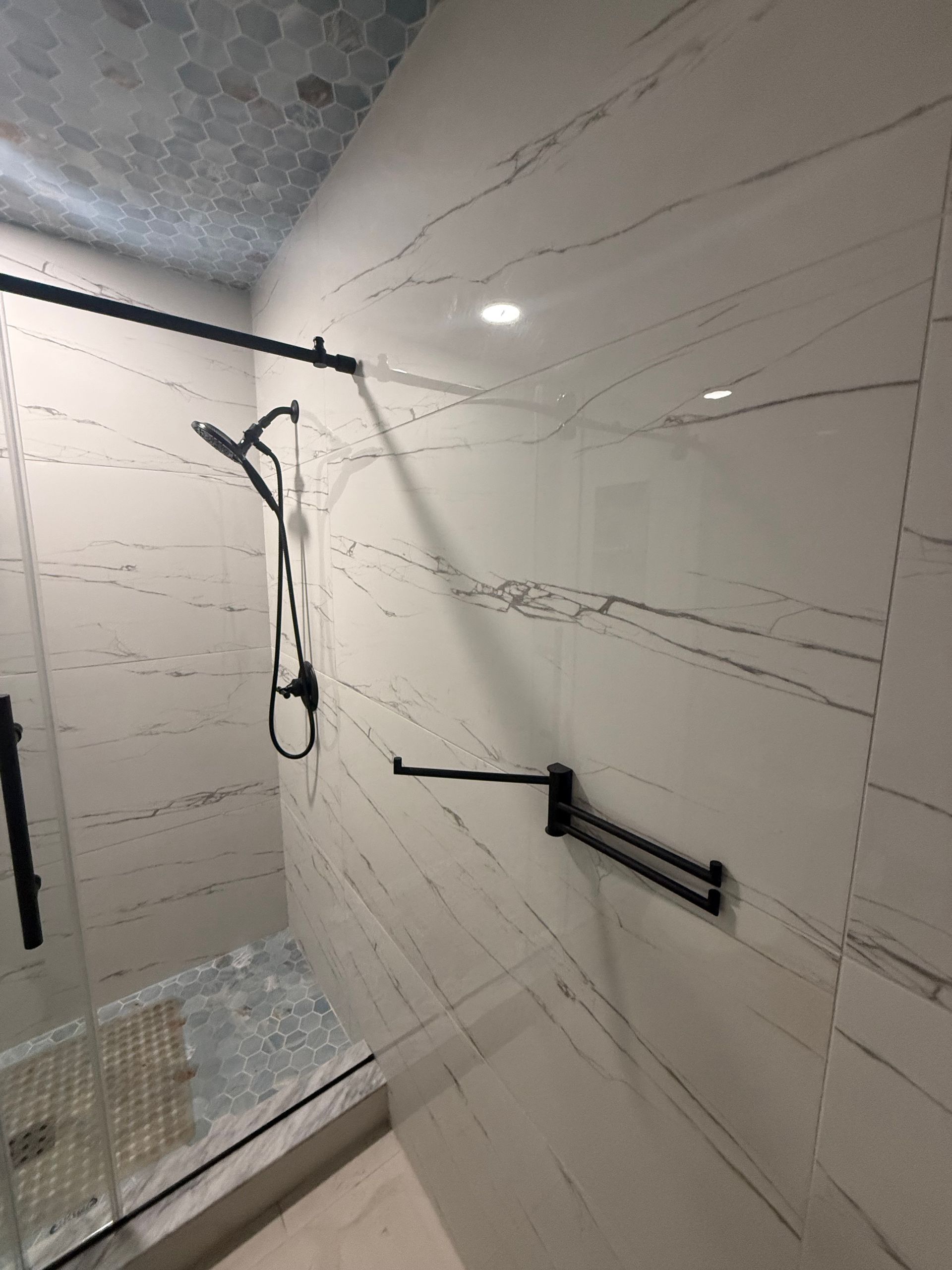 Bathroom with white marble-like tile walls and black fixtures, including a shower head and towel rack.