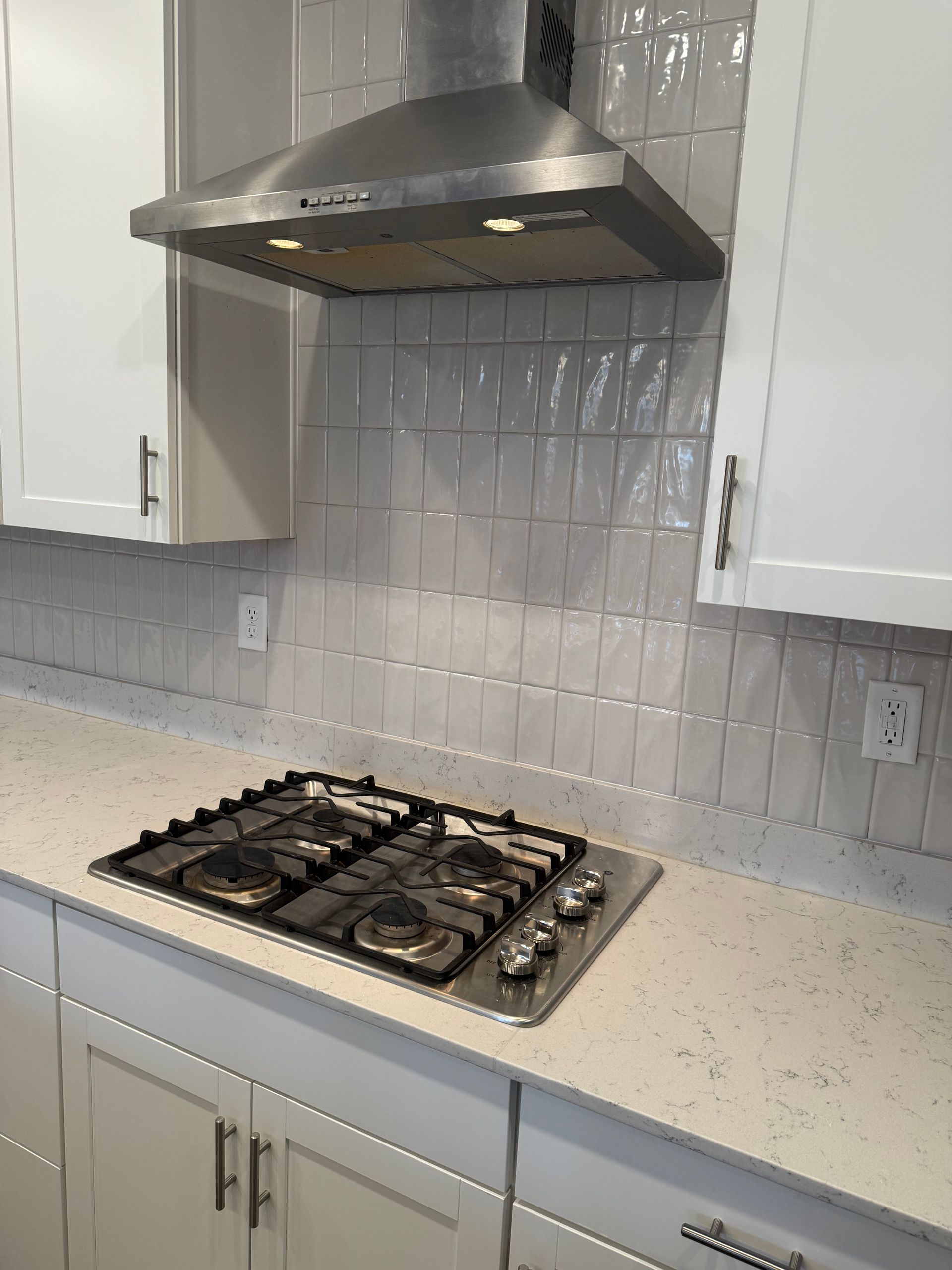 Kitchen with white cabinets, gas stove, stainless steel range hood, and light gray backsplash.