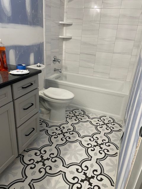 Bathroom with patterned floor tiles, white tub and toilet, gray and white walls, and white vanity with black countertop.