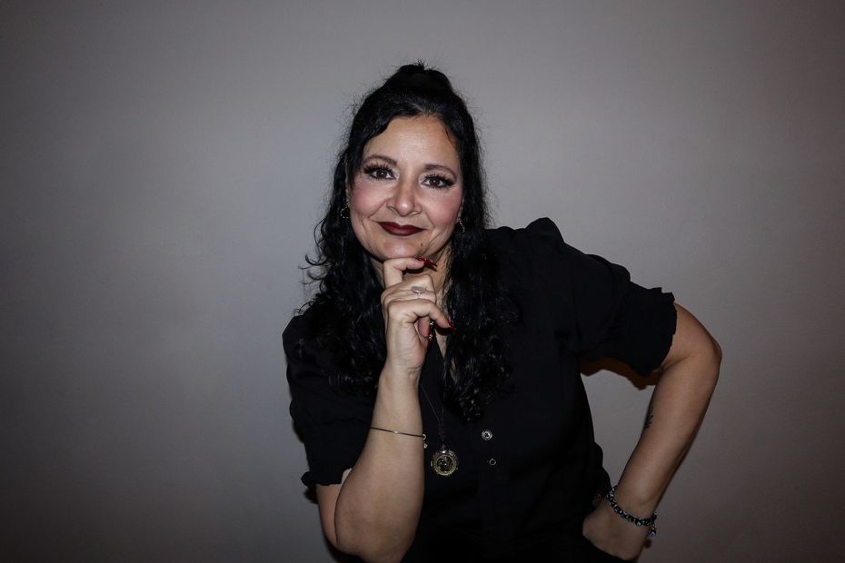 A woman in a black shirt is smiling with her hand on her chin