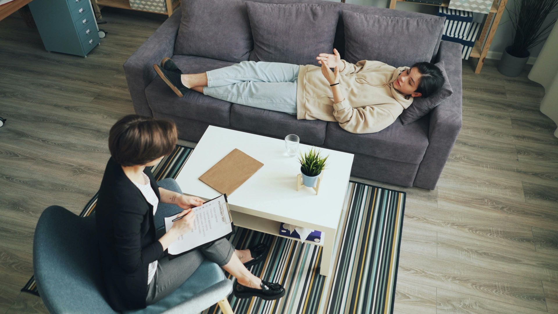 A woman is sitting in a chair talking to a man laying on a couch.