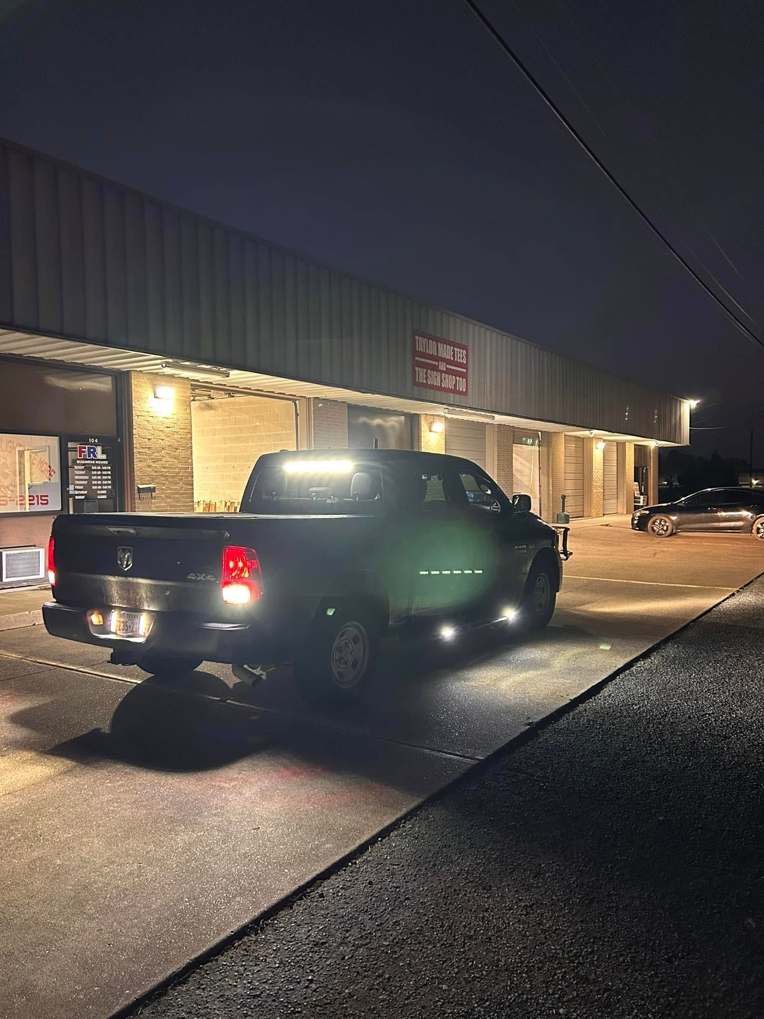 Black pickup truck parked outside a storefront at night. Lights illuminate the vehicle.