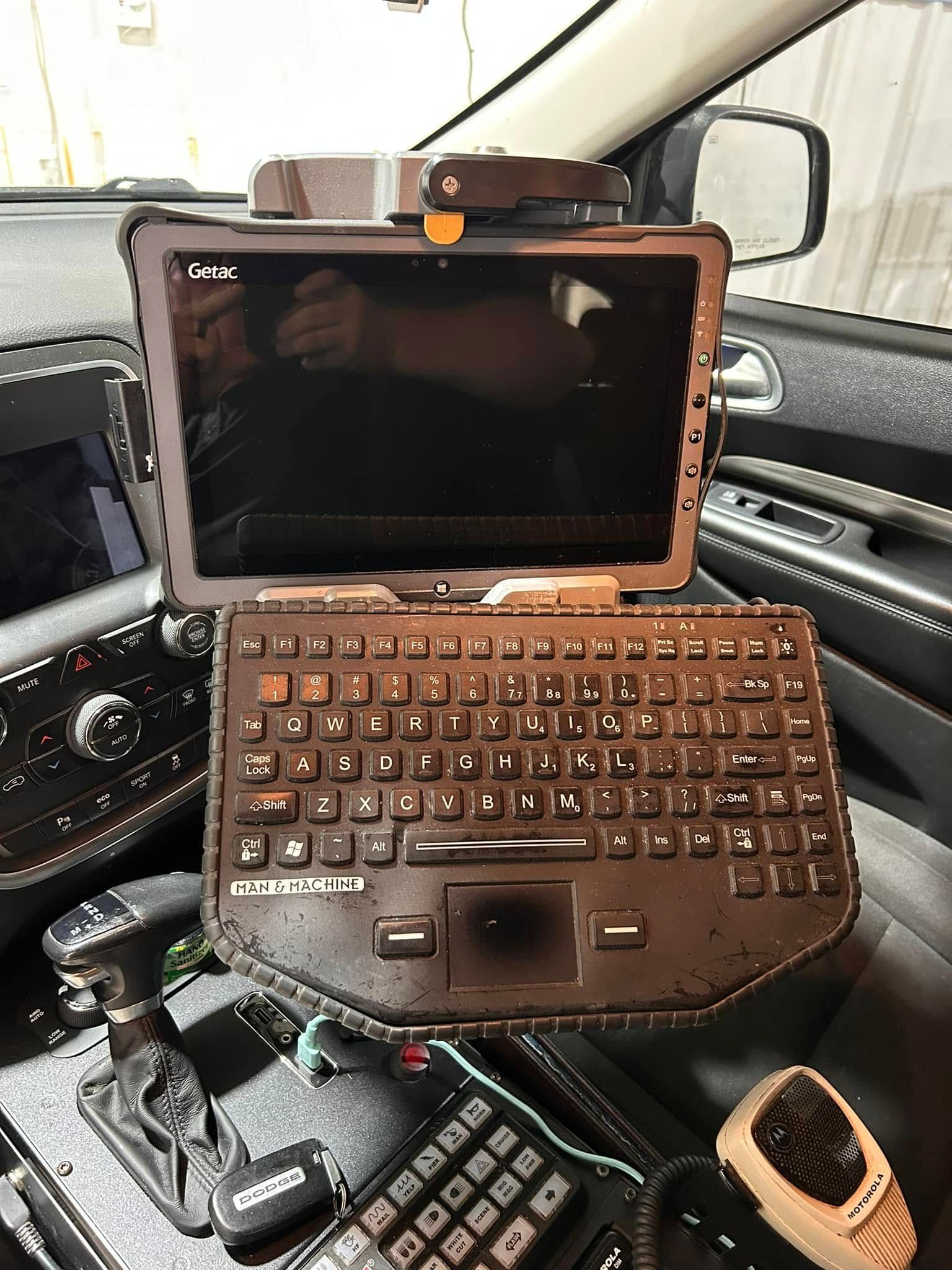 Tablet with keyboard mounted in a vehicle, likely a police car. Black interior with shift lever visible.