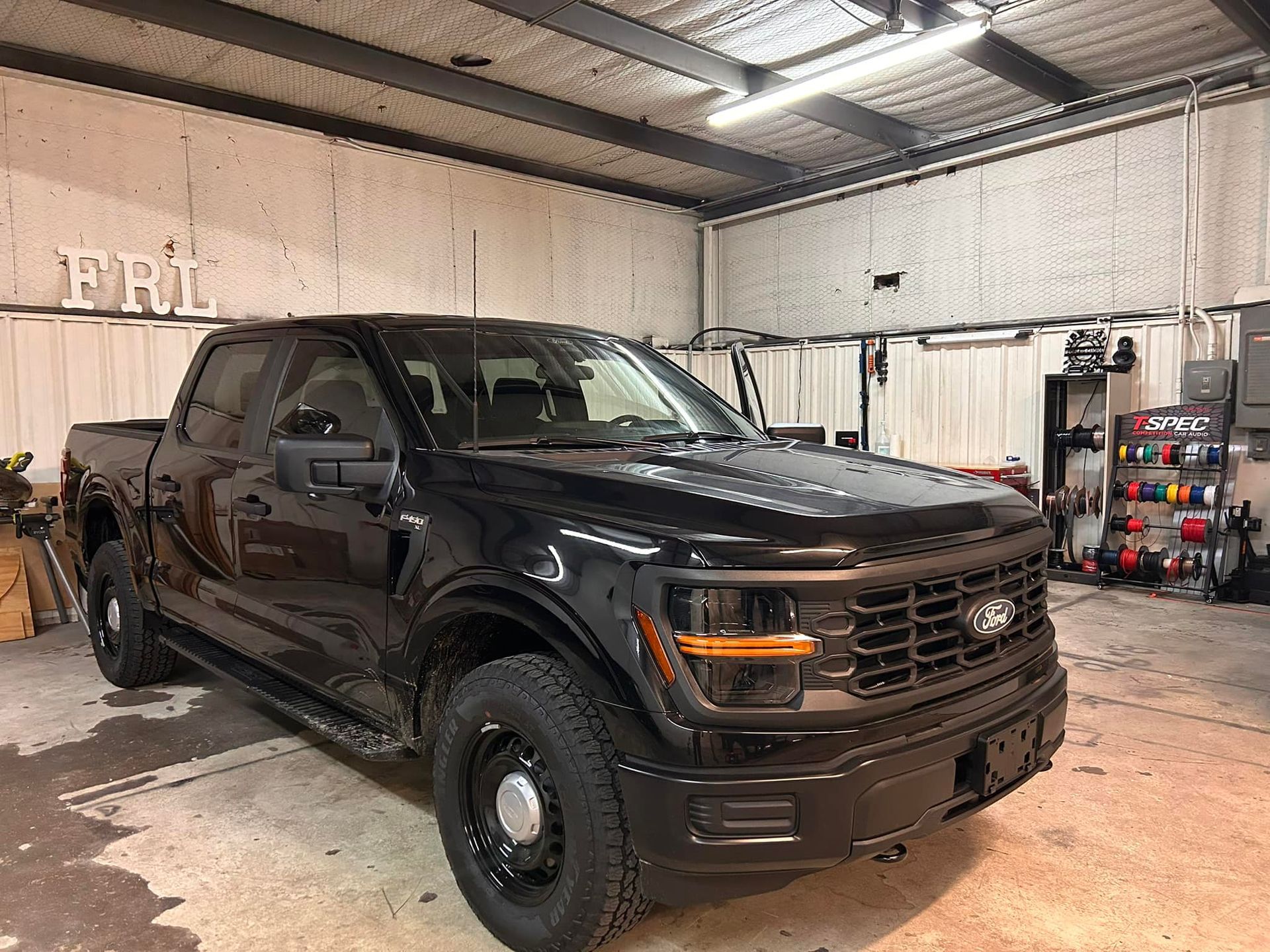 Black Ford F-150 pickup truck parked inside a garage. The truck has black wheels and a black grill.