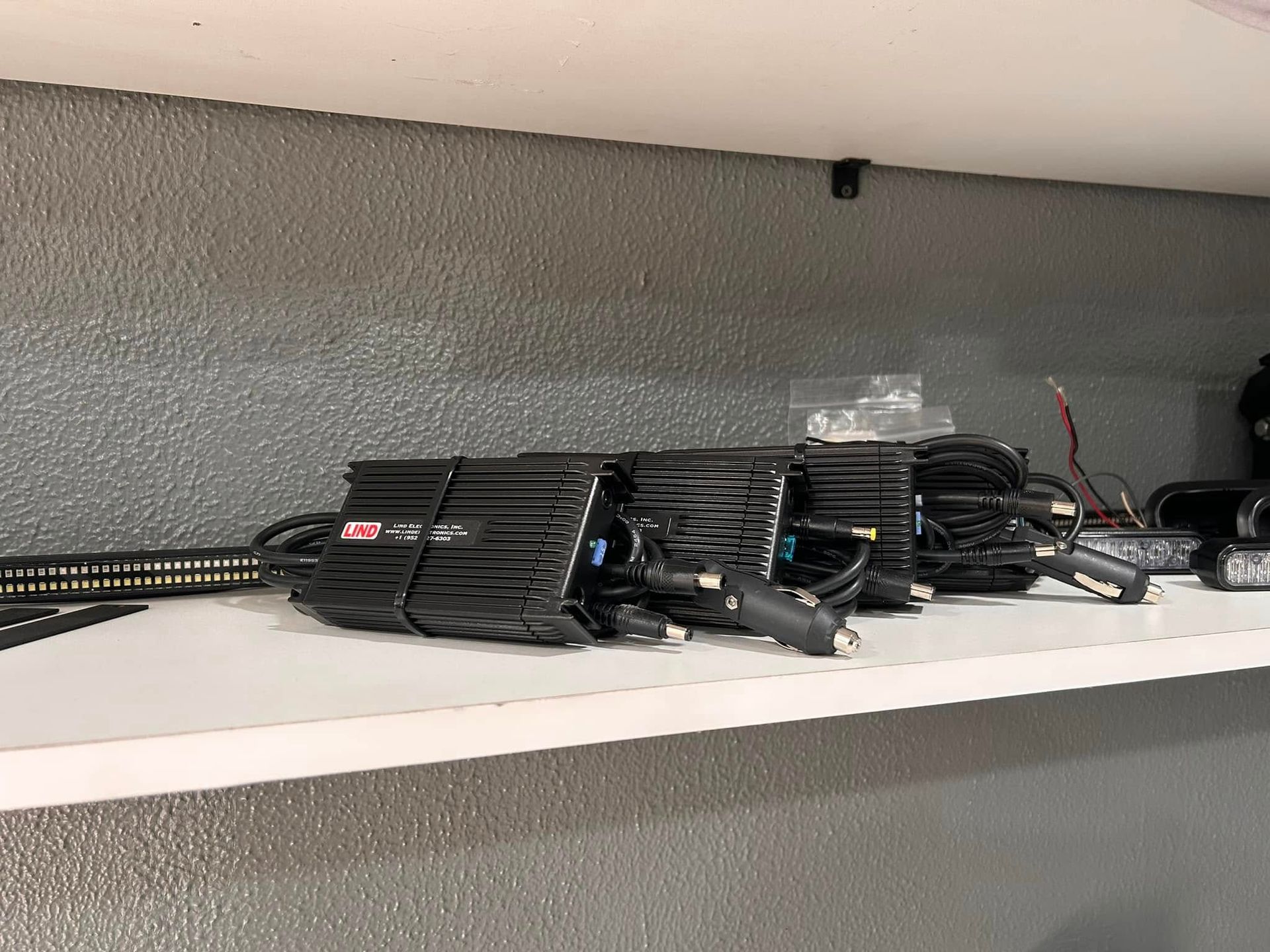 Bundled black electrical components on a white shelf against a textured gray wall.