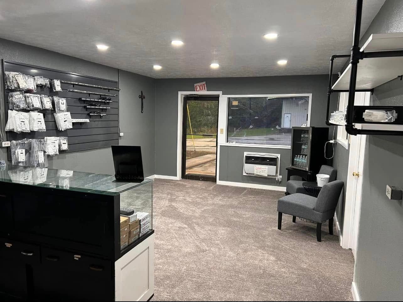 Interior of a store with gray walls, beige carpet, display cases, and a wall of items for sale.