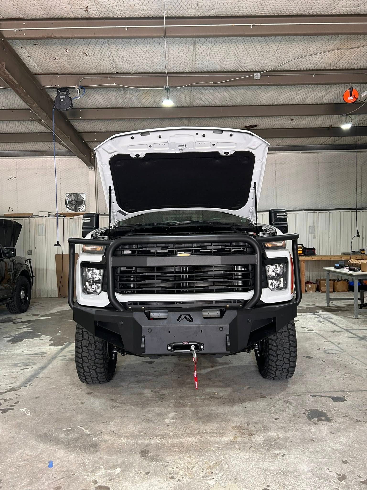 White pickup truck with black grille and bumper, hood open, in a workshop setting.