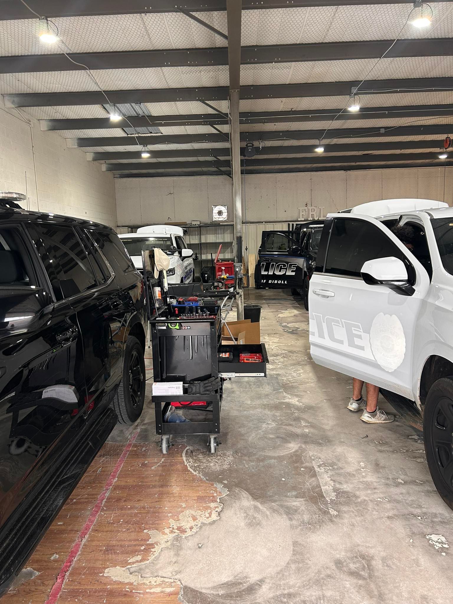 A black SUV and a white police vehicle parked inside a garage workshop with tools and equipment.