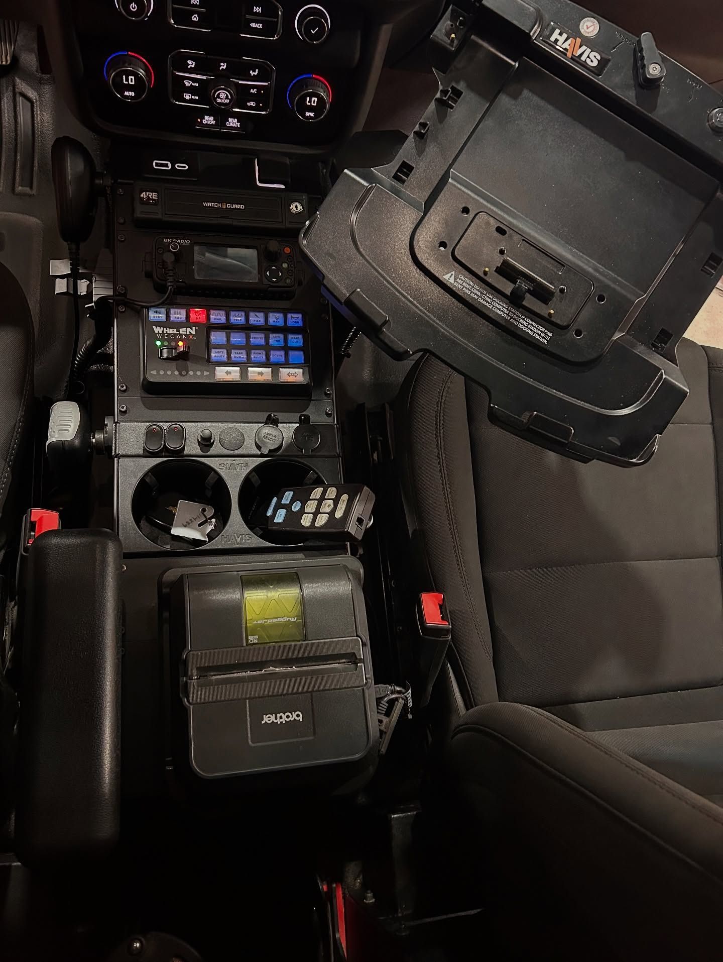 Interior of a police vehicle, center console with equipment, including screen, radio, and storage.